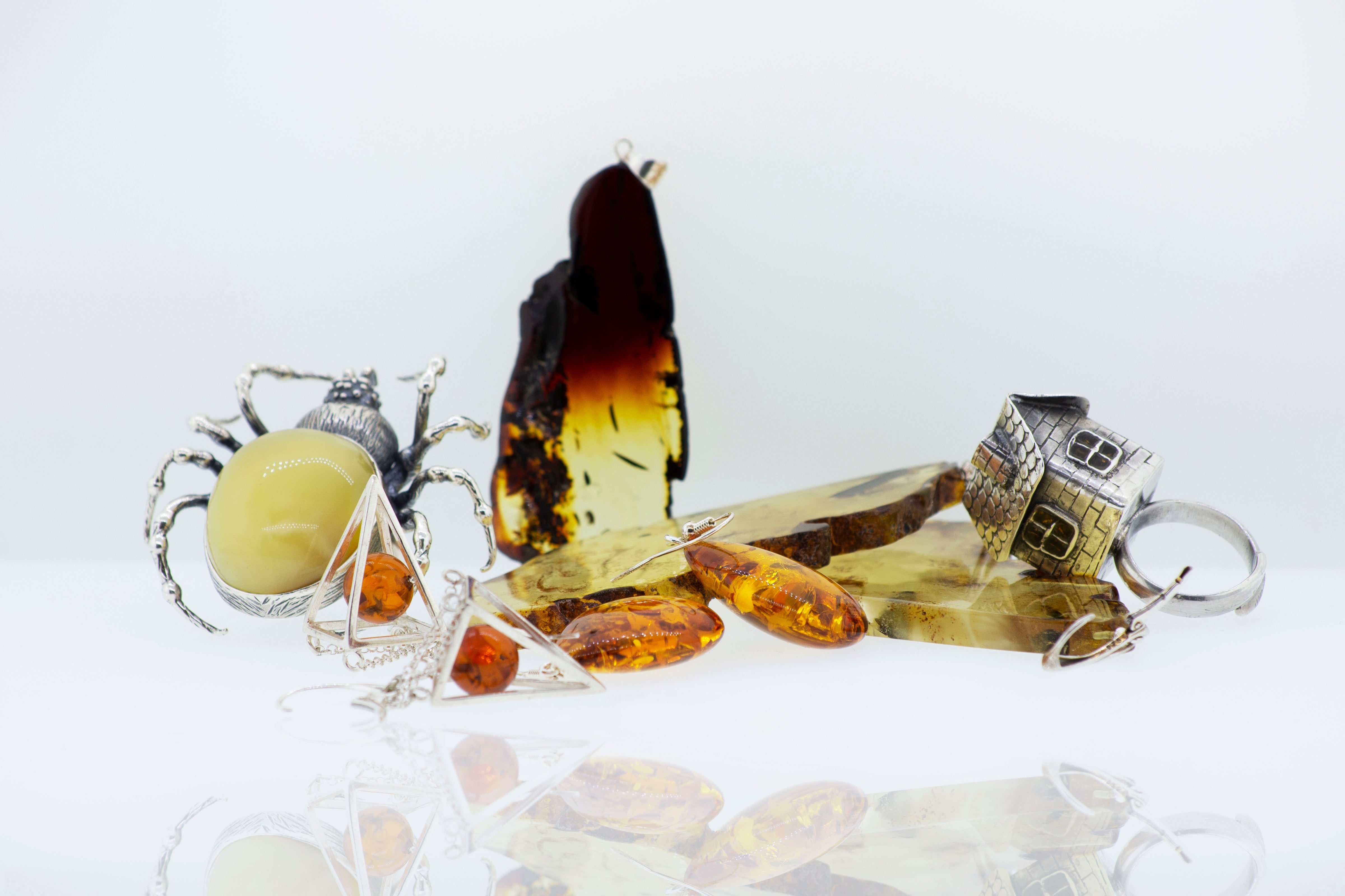 A collection of amber jewelry, including a spider brooch, rings, and pendants, displayed on a reflective surface against a plain background.
