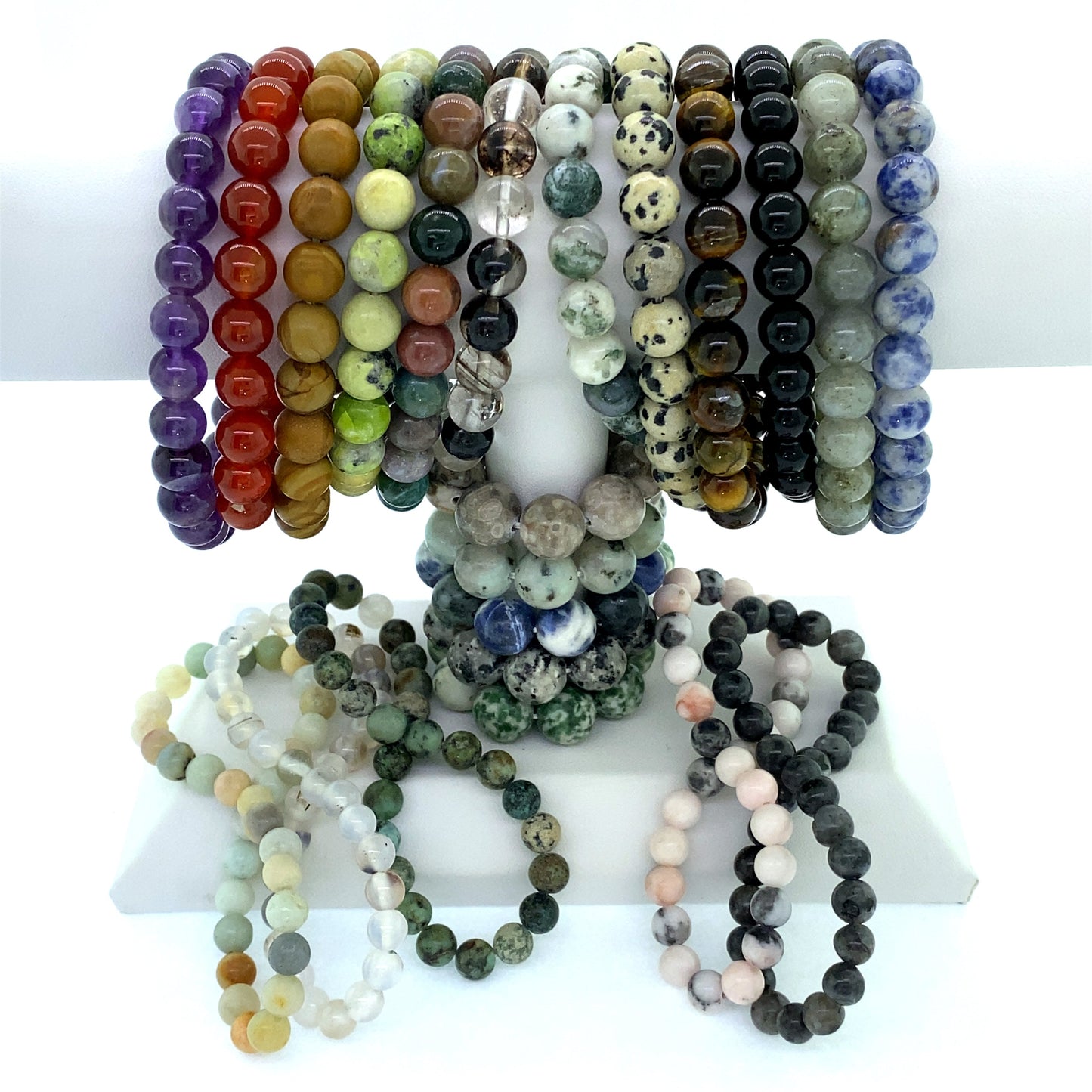 A display of various colorful 4mm Beaded Stone Bracelets arranged on stands, with additional gemstone stackable bracelets draped in front.