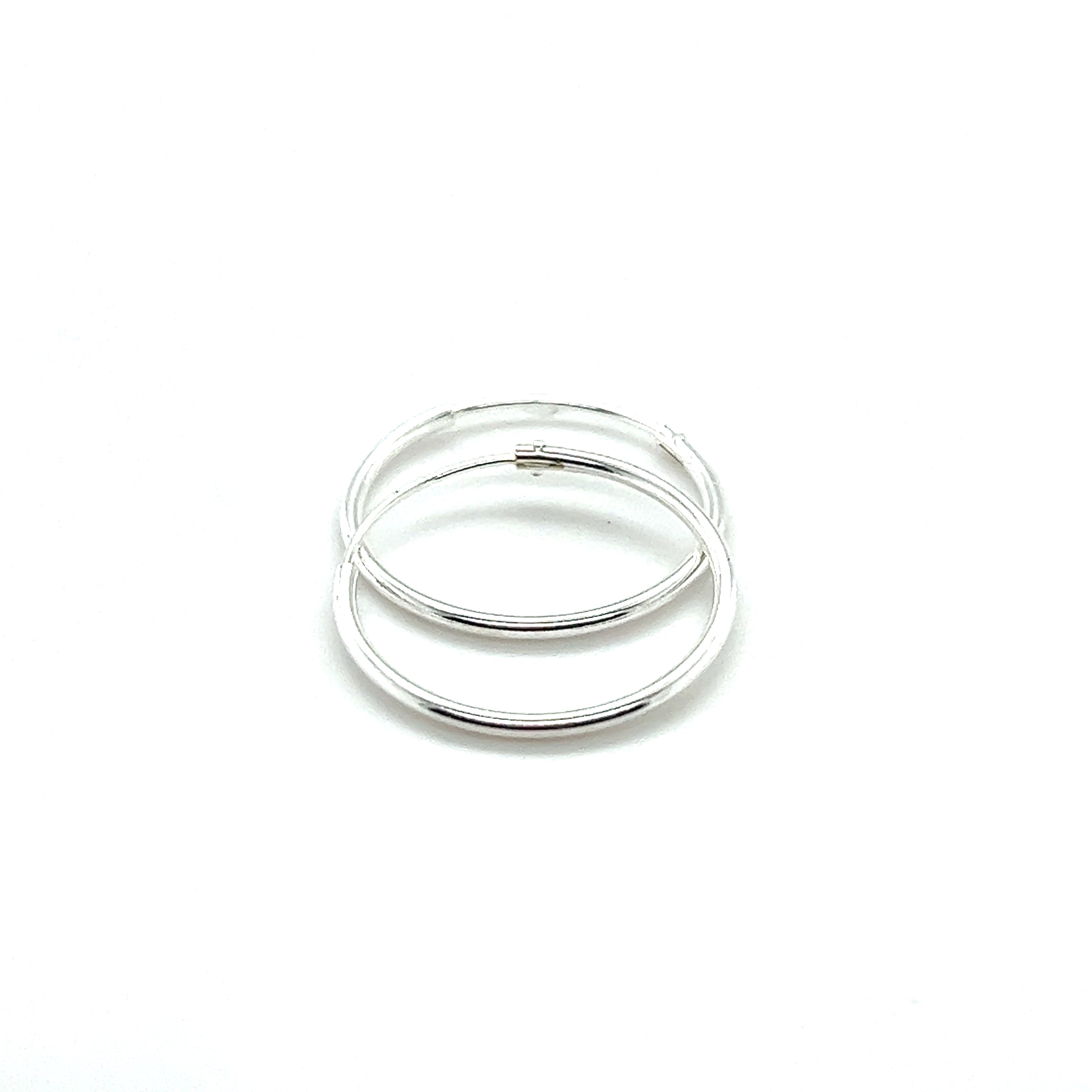 Two 1.2mm Infinity Hoops crafted from .925 Sterling Silver, featuring a subtle infinity design, are elegantly displayed on a white background.