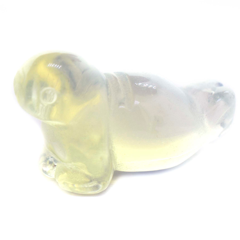 A Carved Opalite Seal Figure sitting on a white surface, capturing the playful essence of the ocean.