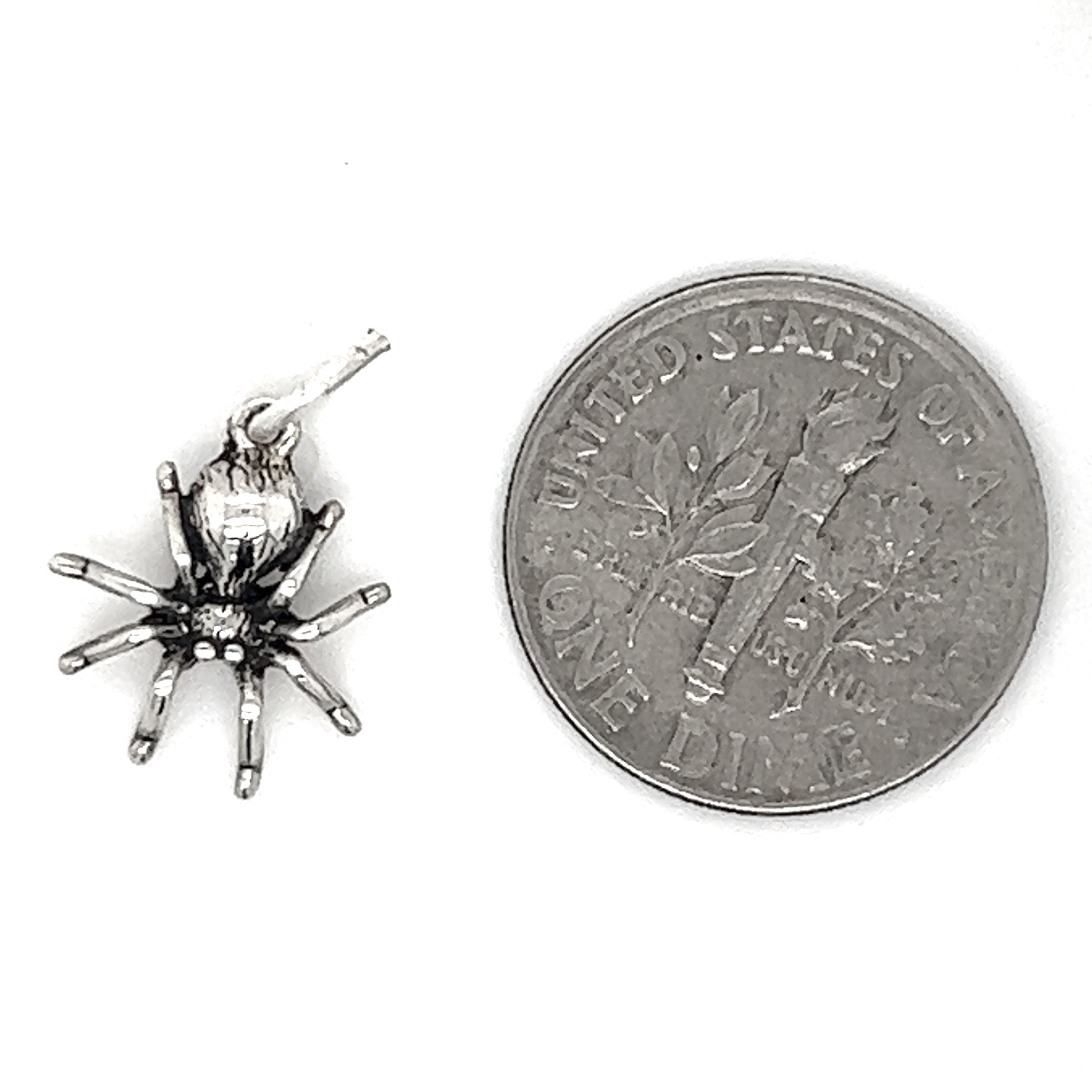 A silver Tiny Haunting Spider Charm resting next to a penny, exuding spooky witch vibes.