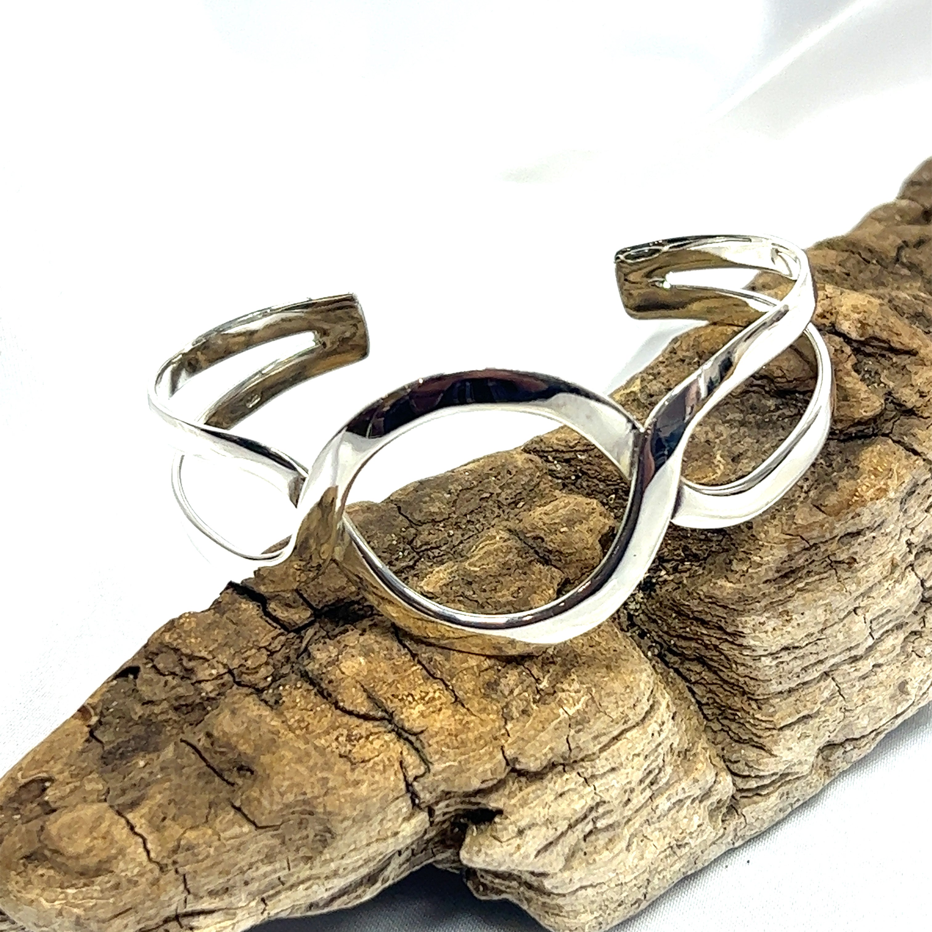 A Trendy Twisted Cuff with Circle Design bracelet made of Super Silver adorns a piece of wood.