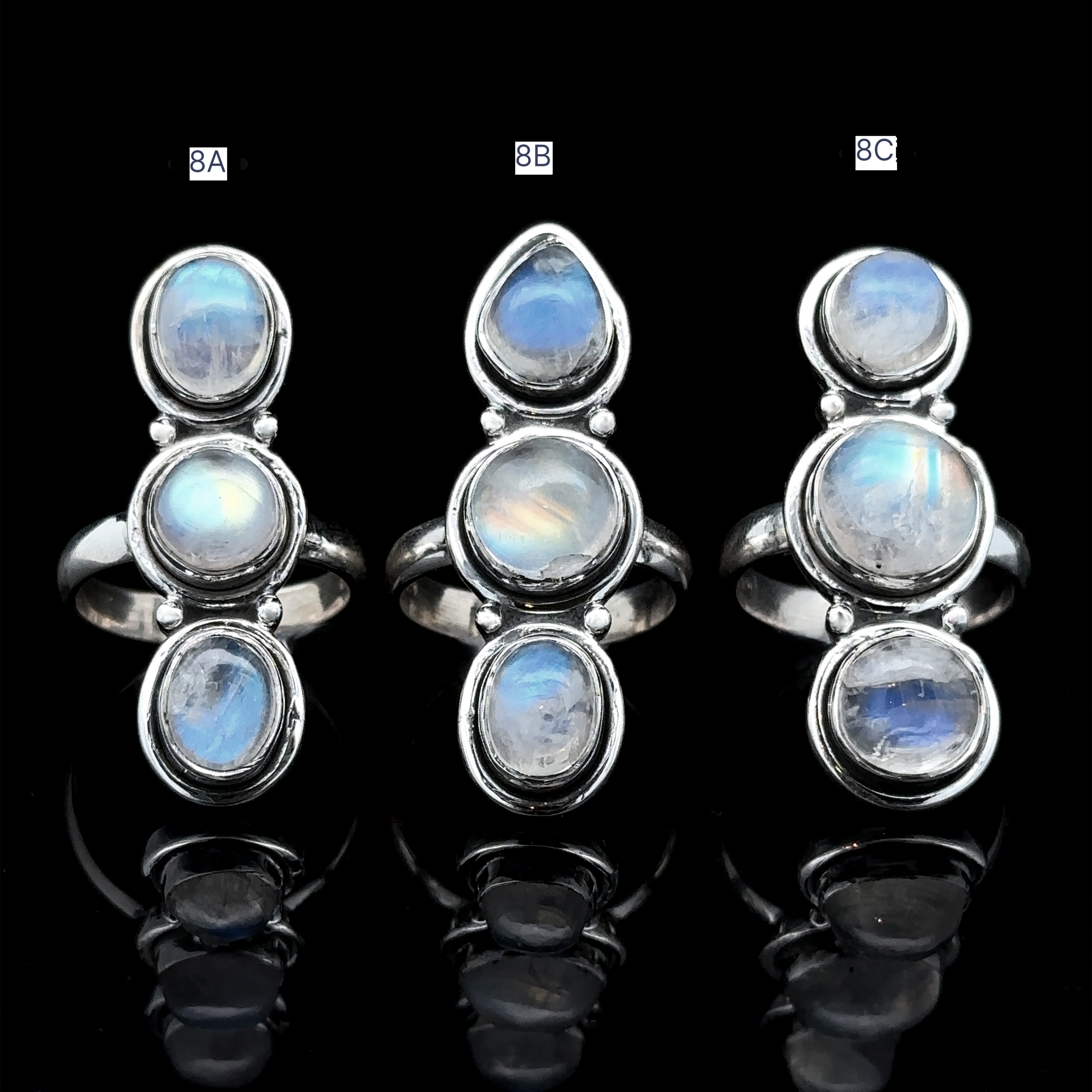 The Triple Moonstone Ring, featuring three sterling silver rings with oval moonstone settings labeled 8A, 8B, and 8C, is showcased against a black background and radiates goddess energy.