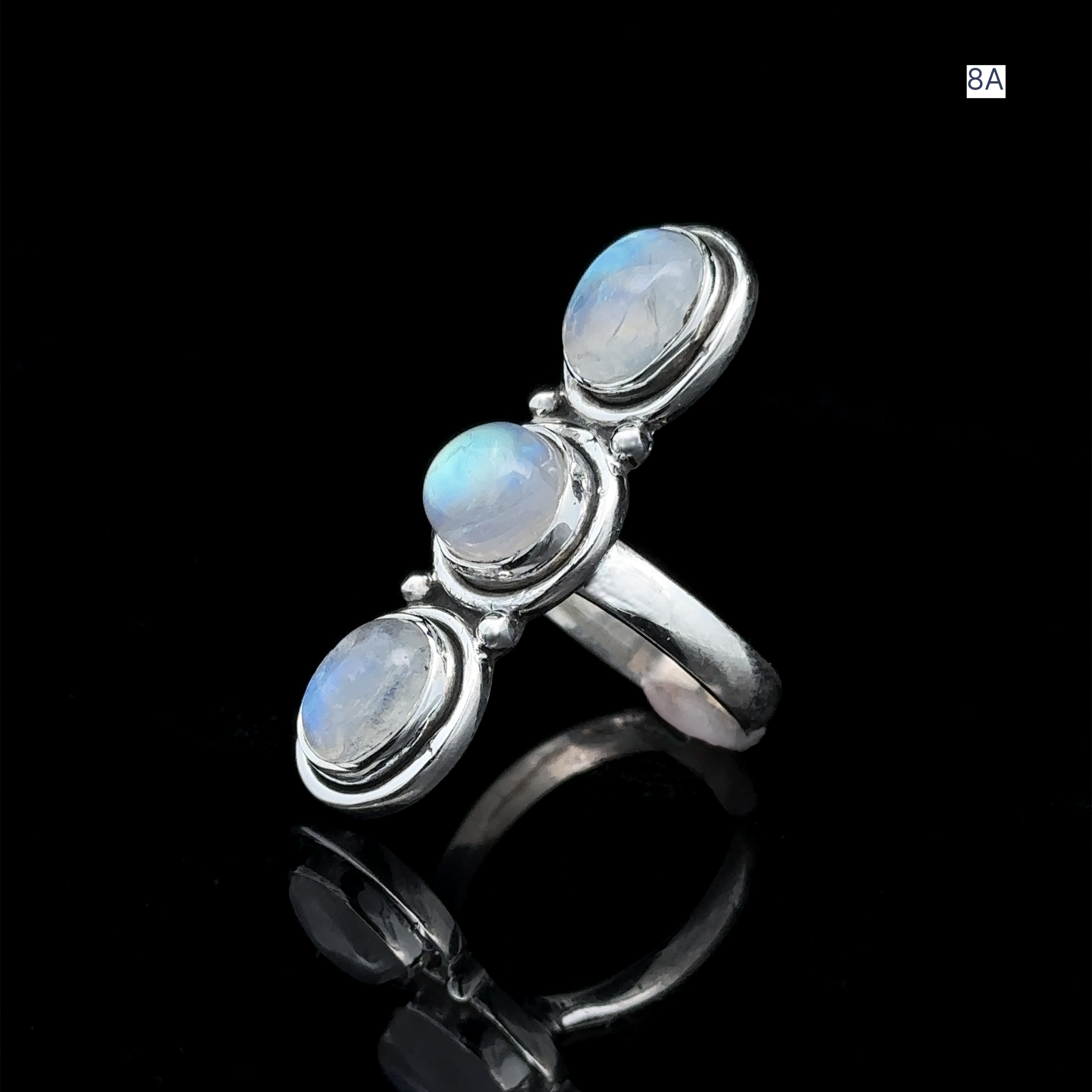 Triple Moonstone Ring made of sterling silver, adorned with three round blue gemstones, is elegantly showcased on a reflective black surface, exuding goddess energy.