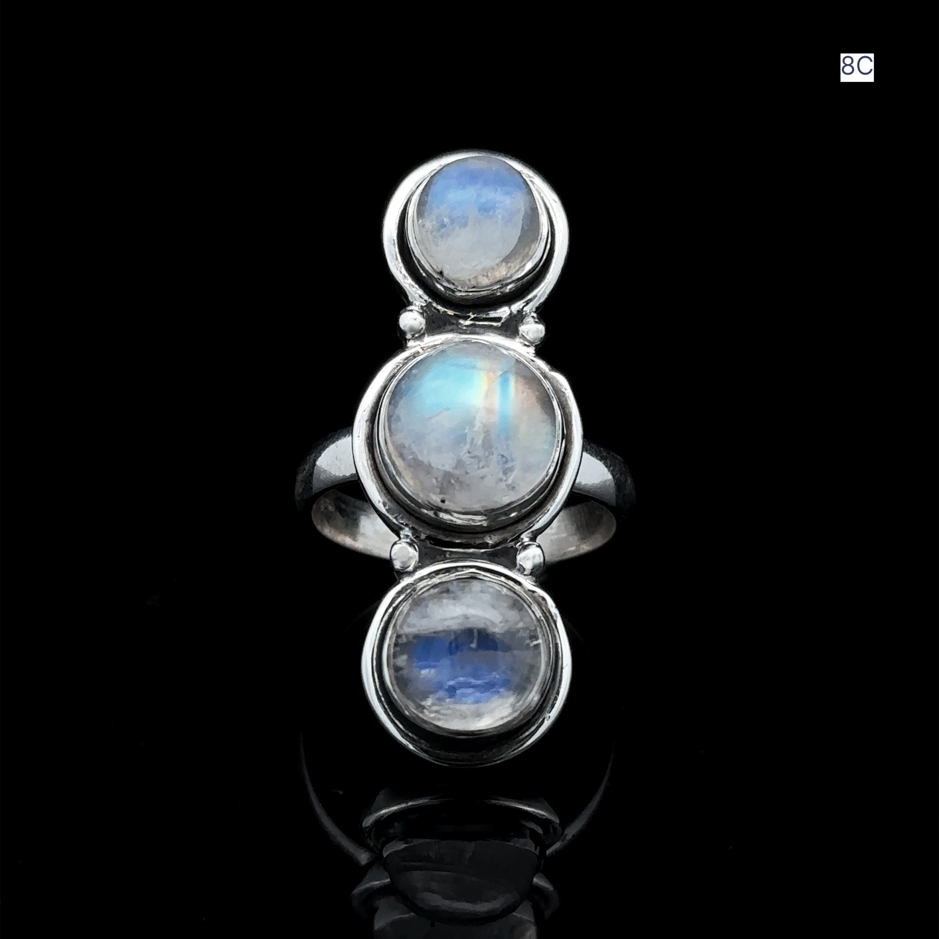 The Triple Moonstone Ring, crafted from sterling silver and featuring three round moonstone settings, exudes goddess energy as it gleams against a black background.