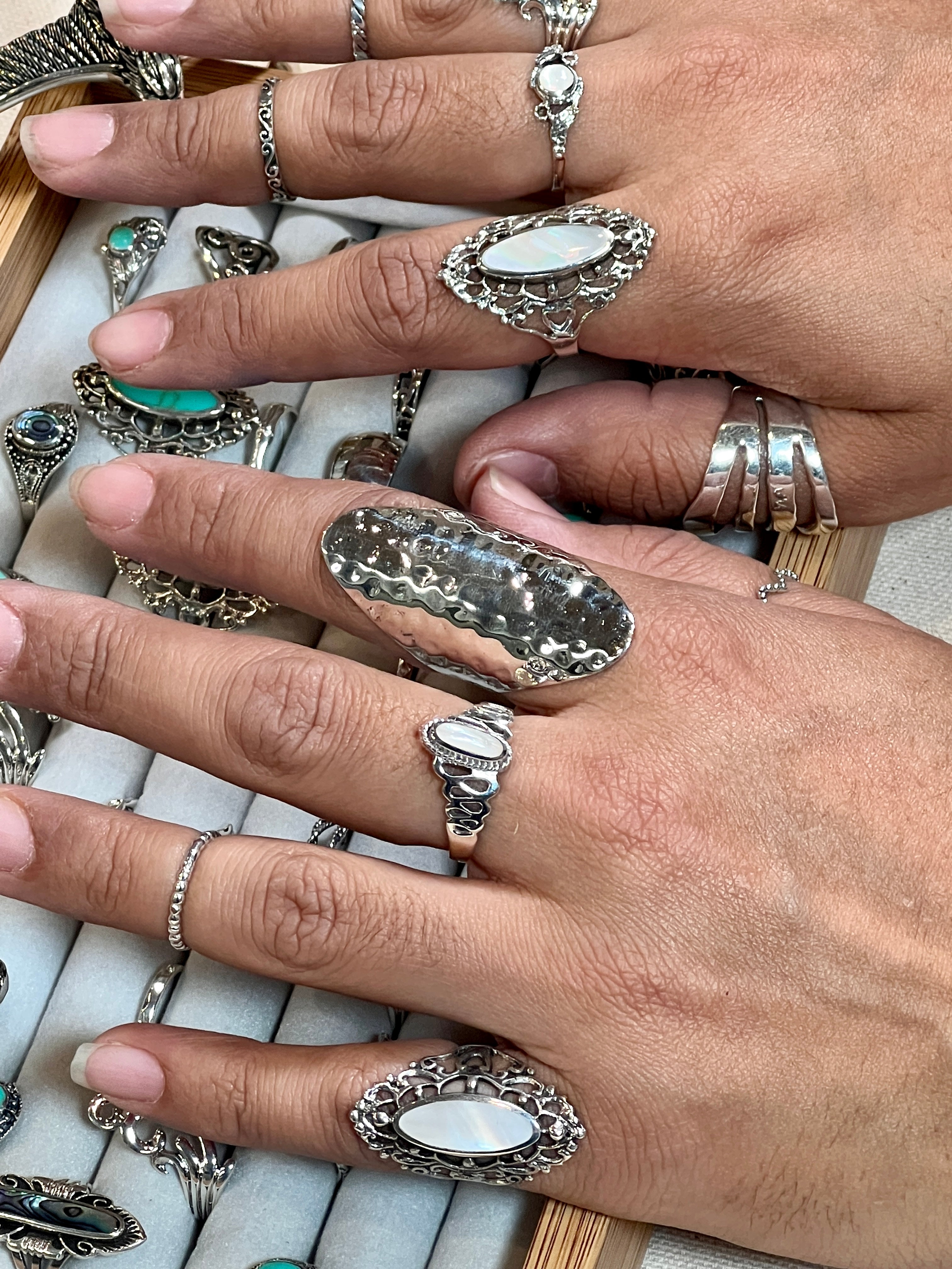 A woman's hands showcasing the Super Silver Oval Inlaid Stone Ring With Wavy Squiggle Design, featuring exquisite Mother Of Pearl accents. Crafted with impeccable skill and elegance, these rings are crafted with the highest quality .925 Sterling.