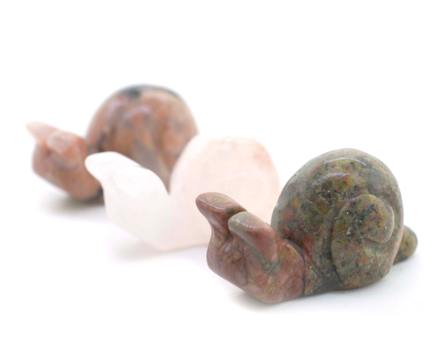 Three small Snail Carved Gemstone Figures sitting on a white surface, adding decoration to any space with their vibrant green color.