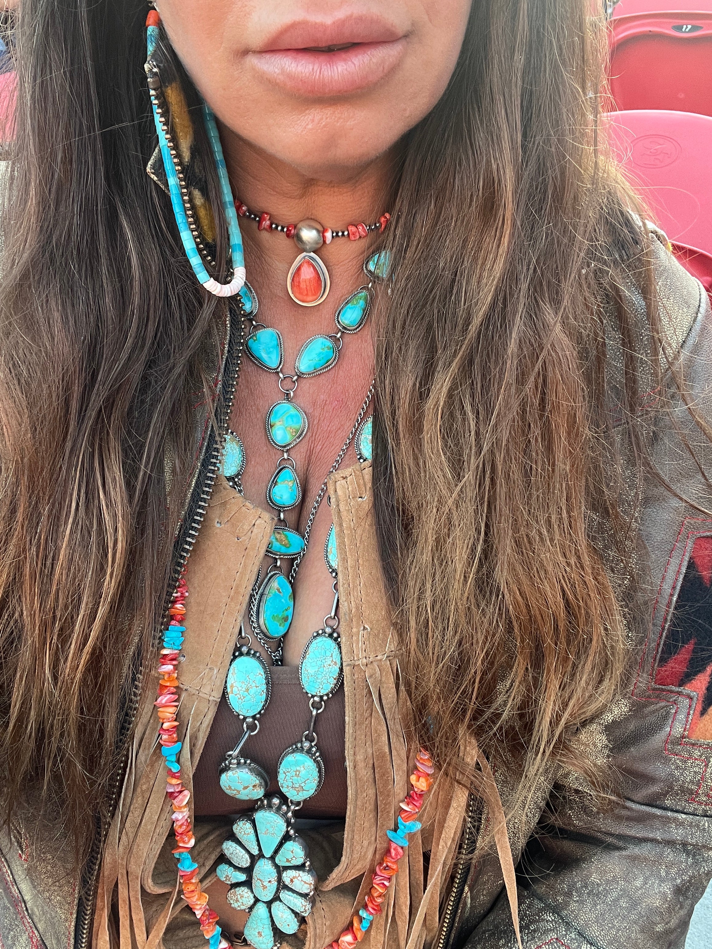 A person with long hair wearing a Stunning Sonora Gold Lariat Necklace And Earrings Set, a brown fringed top, and a jacket featuring an authentic Native American handmade textured rope design.