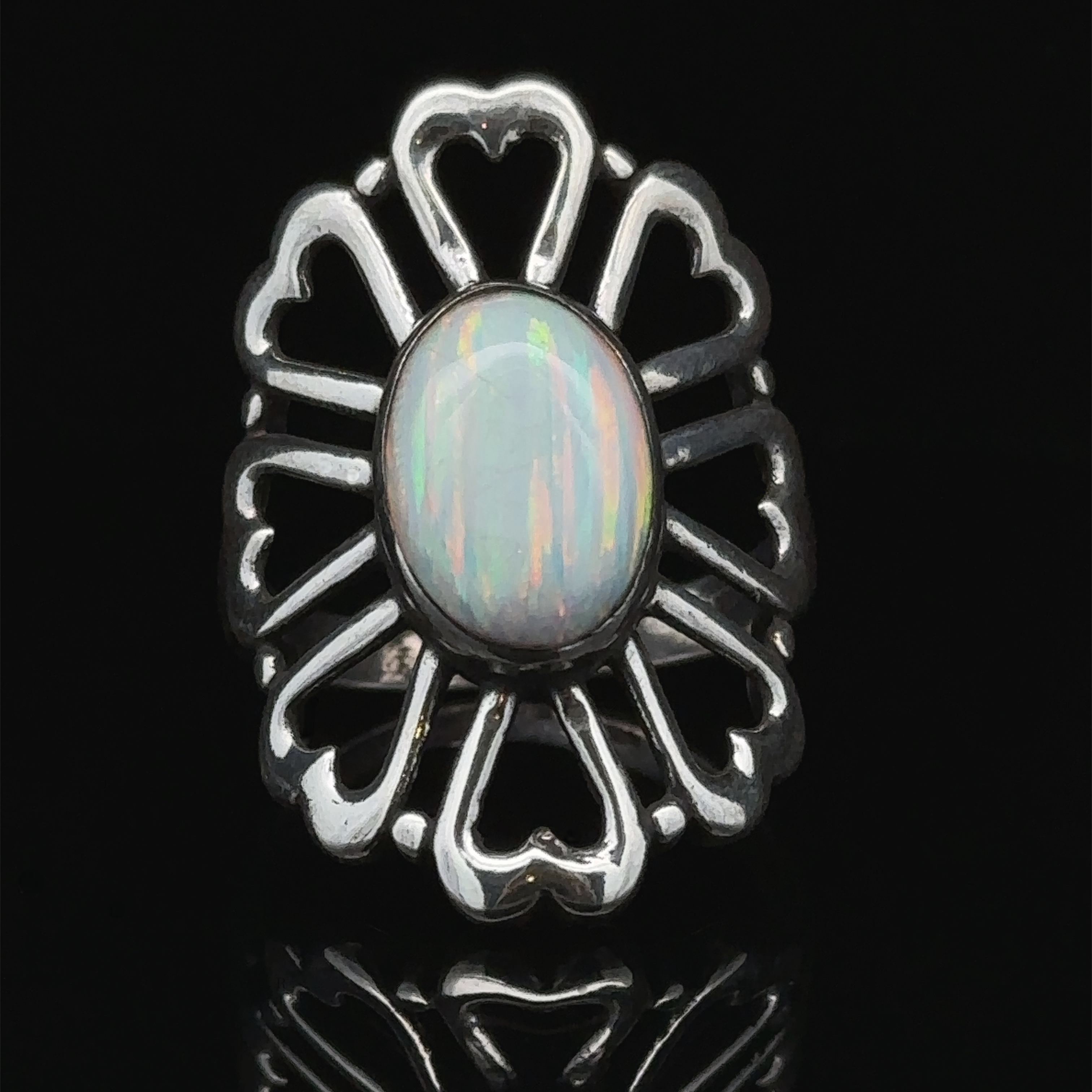 An American Made Opal Flower Ring with Heart Shaped Petals is set in an ornate heart-shaped design against a black background, handcrafted in America.