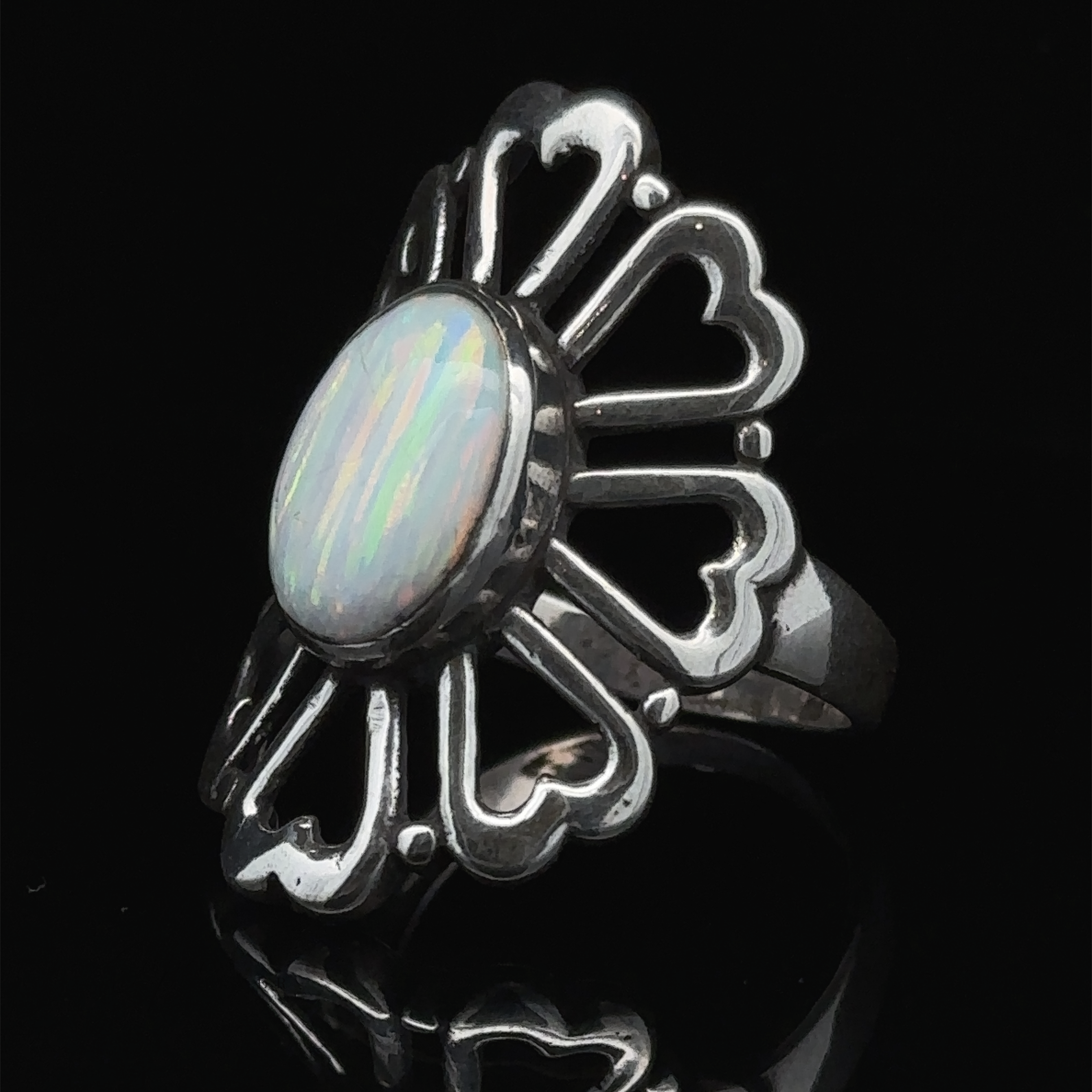 The American Made Opal Flower Ring with Heart Shaped Petals, featuring a central oval opal gemstone on a black background, handcrafted in America.
