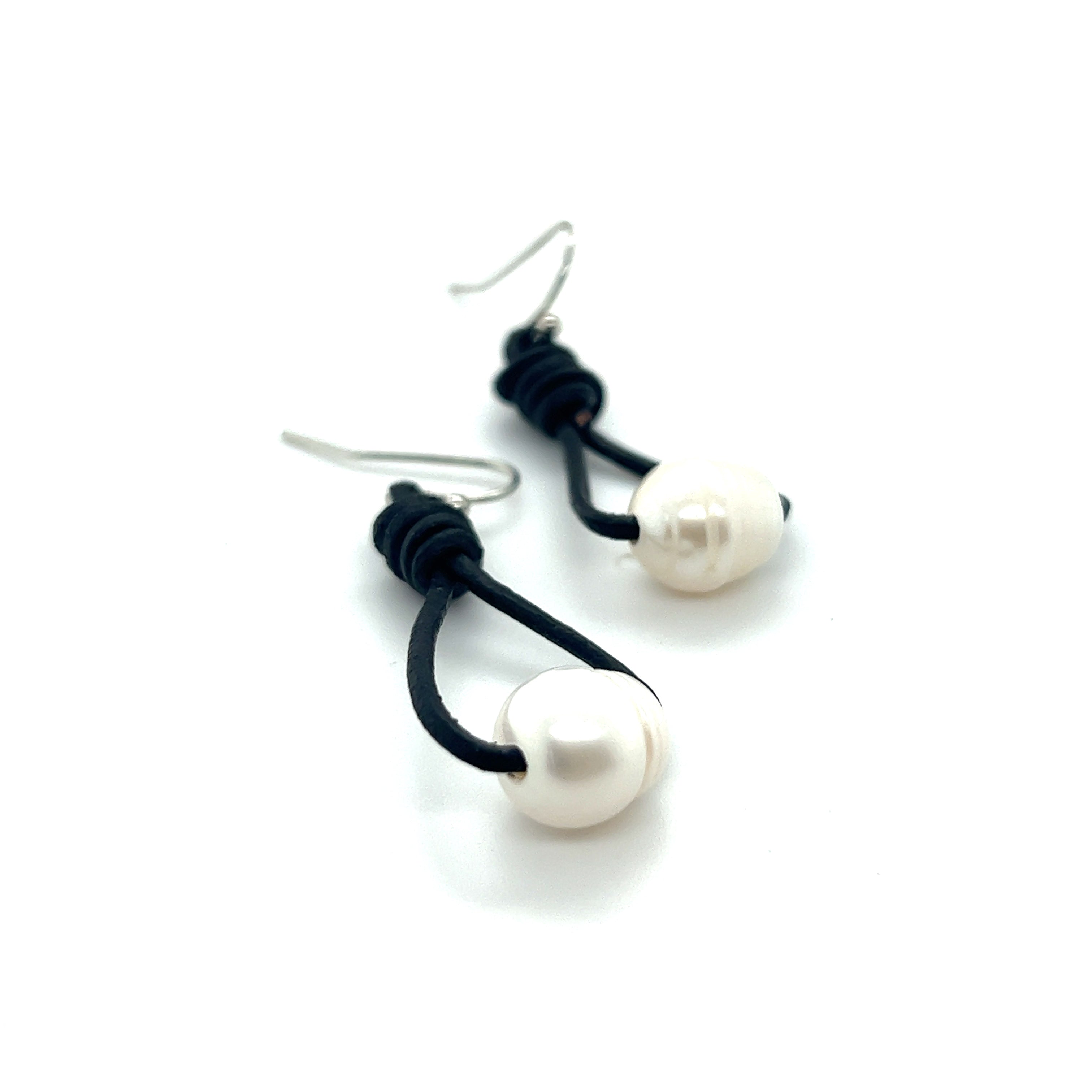 A pair of Super Silver Leather Cord and Pearl Earrings with a laid-back style on a white surface.