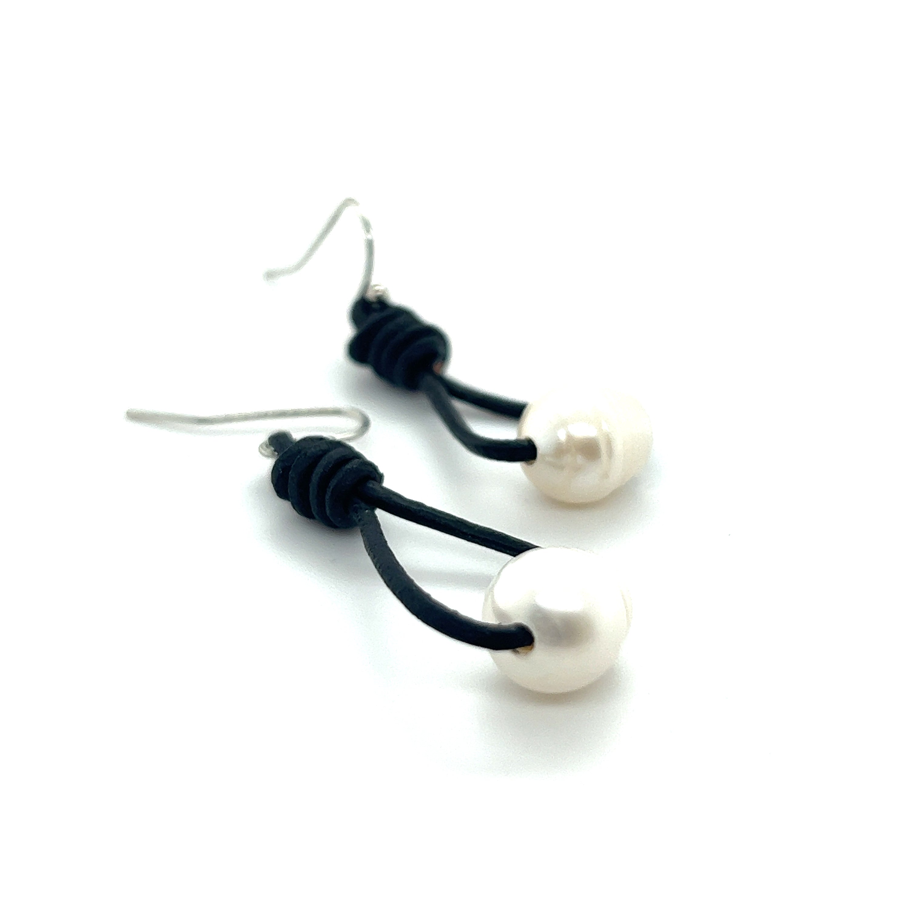 A pair of Super Silver Leather Cord and Pearl Earrings on a white surface, with a laid-back style.