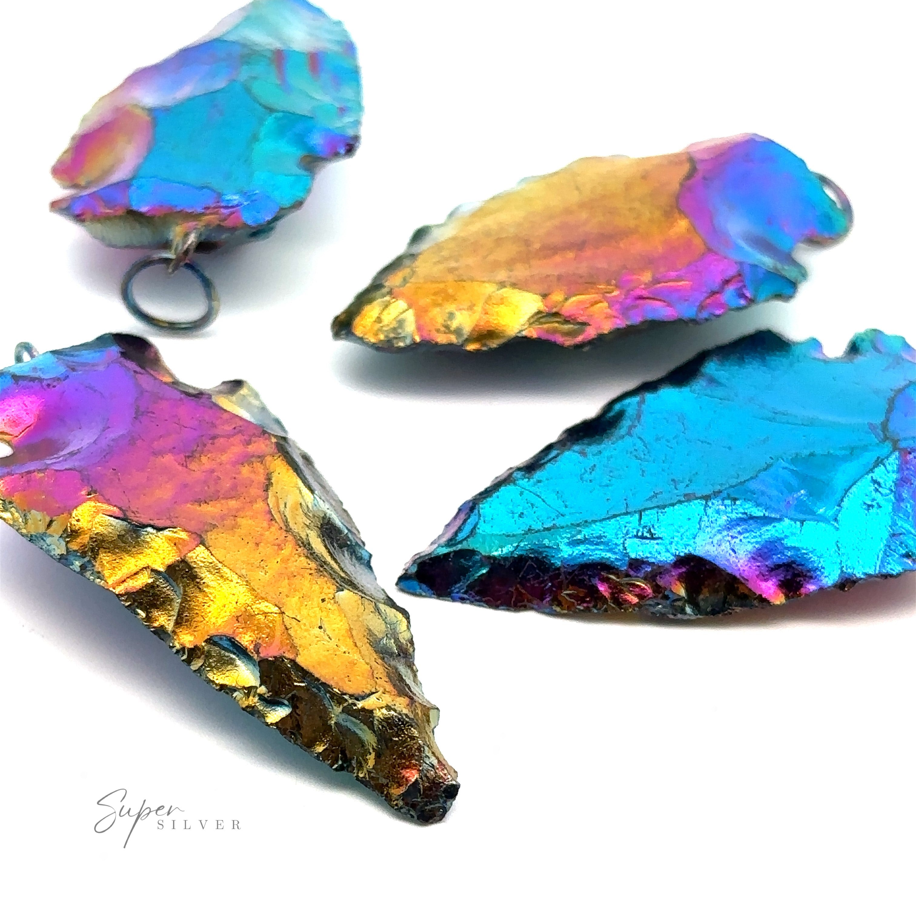 Four Rainbow Hematite Arrowhead Pendants in blue, pink, and gold hues are arranged on a white background.