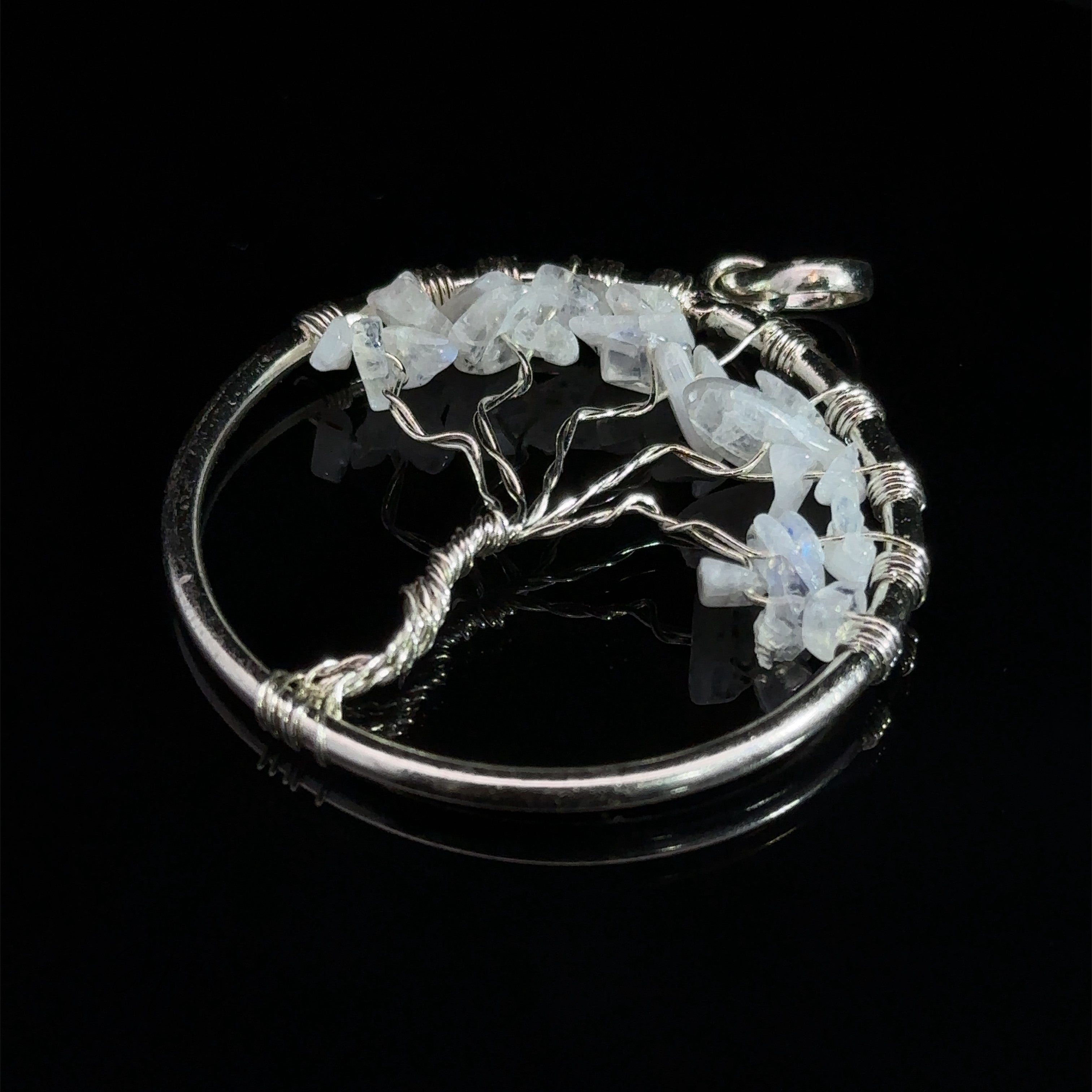 A circular silver Wire Wrapped Tree of Life Pendant with Stones features a design with branches adorned with translucent white gemstones. The black background highlights the intricate details of the wire-wrapped pendant.