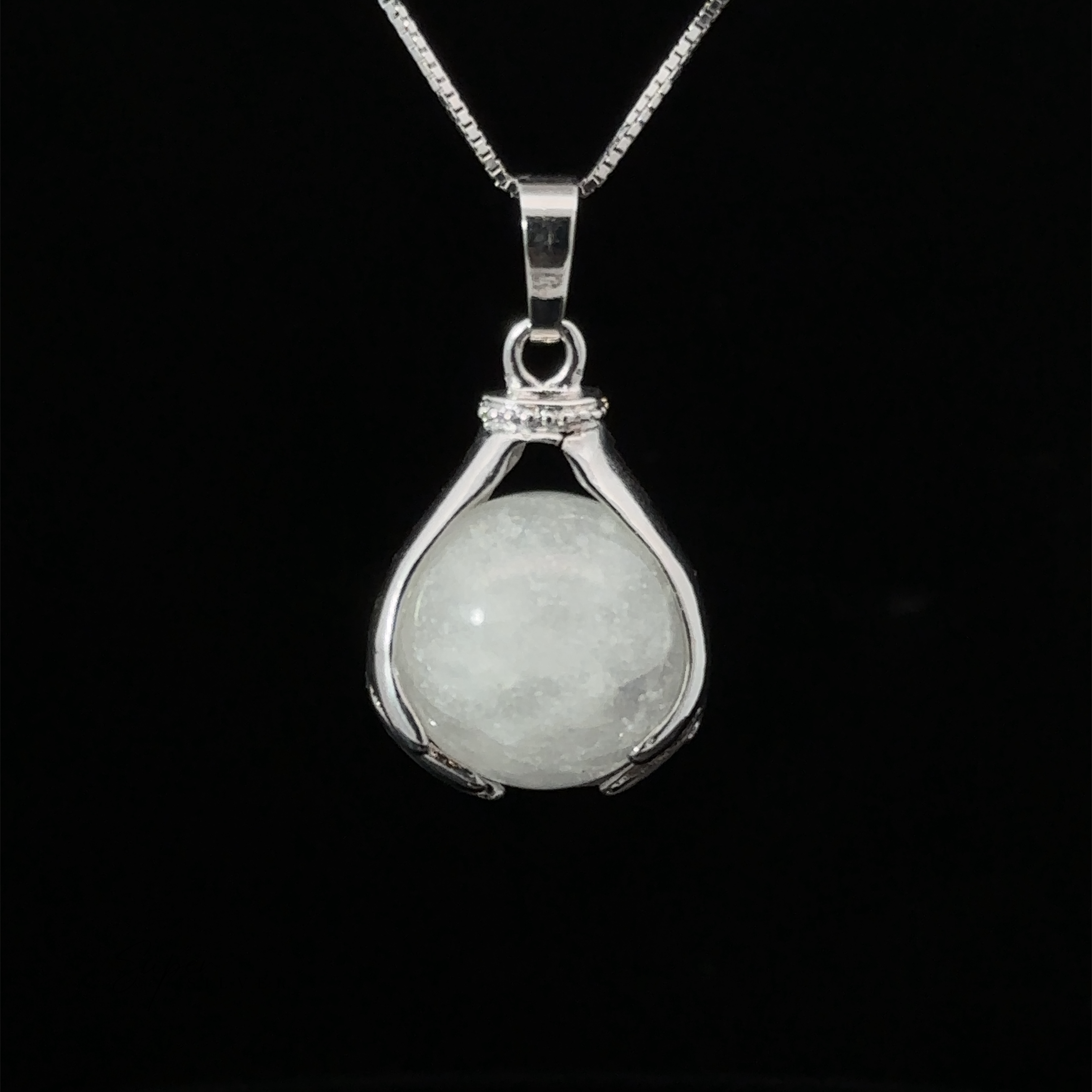 A Sphere Crystal Pendant features a smooth, round quartz gemstone held between two curved prongs, suspended from a thin chain against a black background.
