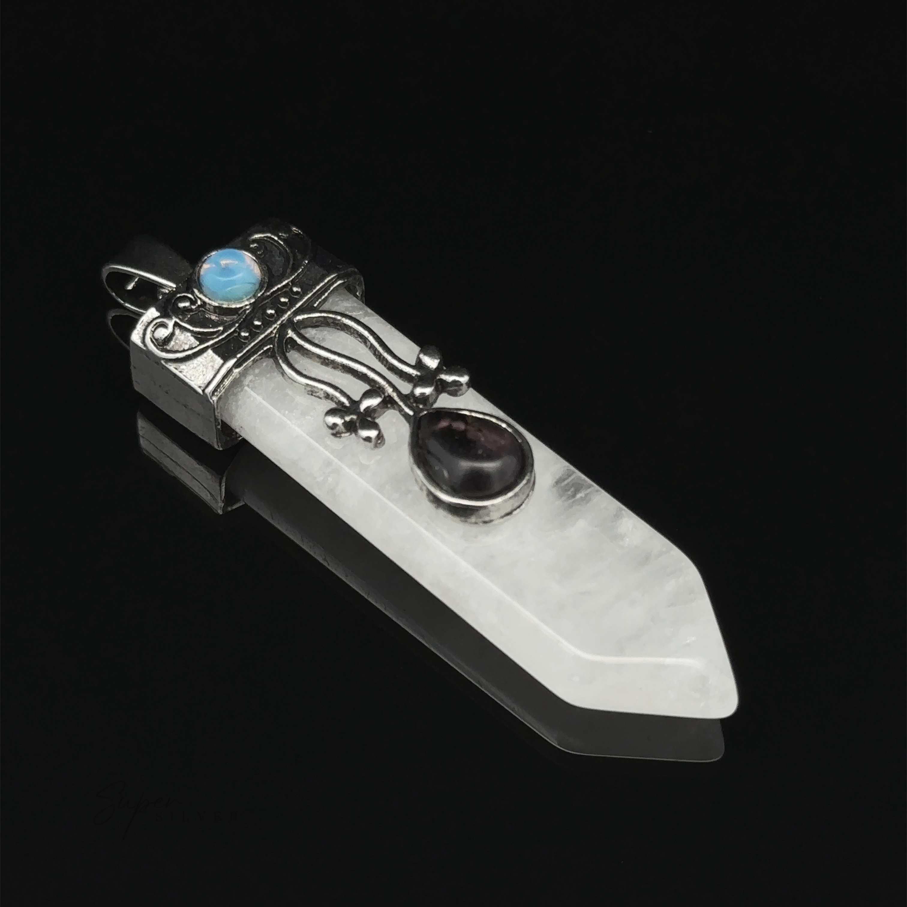 A pointed, clear crystal pendant with silver decorative metalwork, featuring a small blue stone and a larger dark stone, lies against a black background. This Obelisk Crystal Stone Pendant exudes elegance and mystical charm.