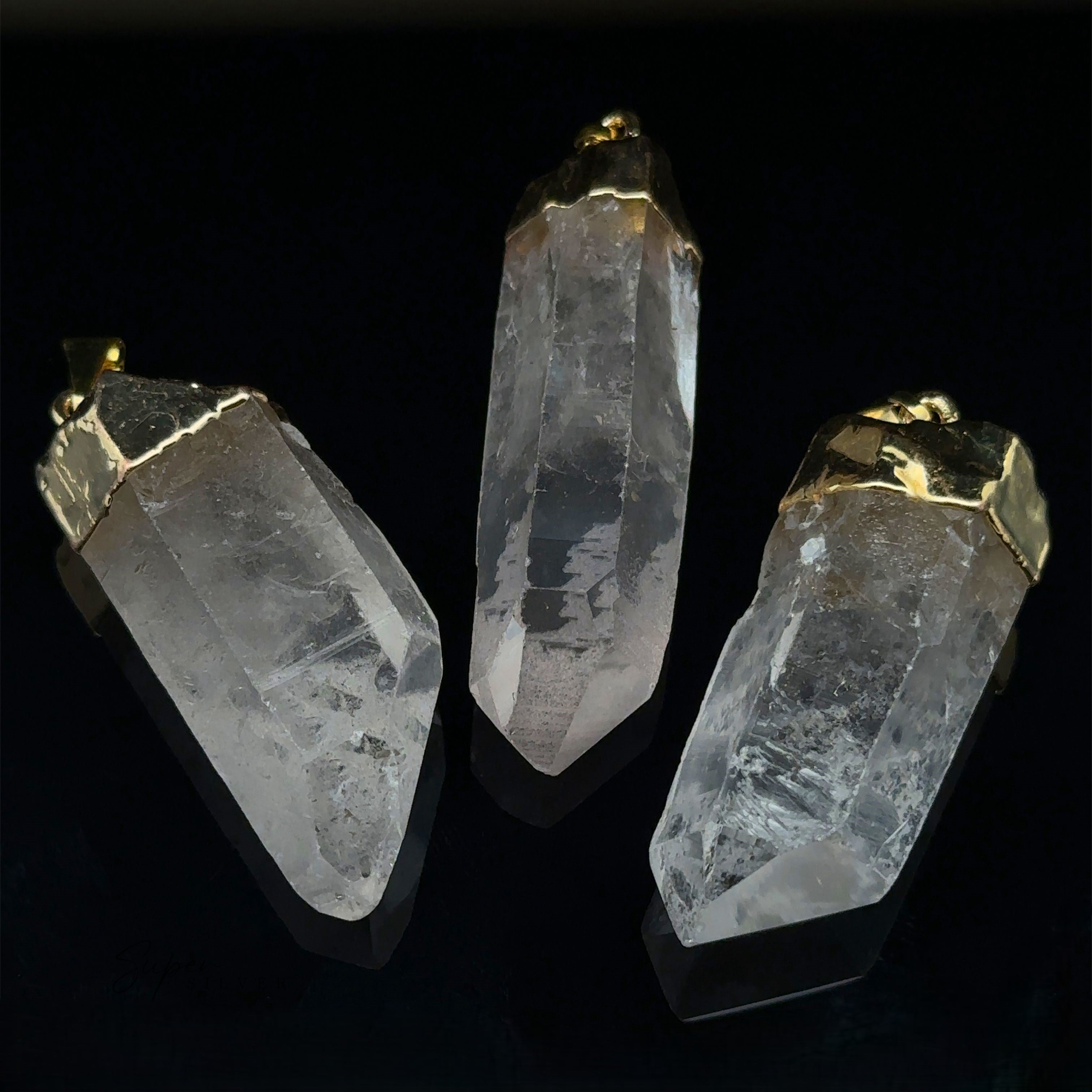 Three Raw Crystal Pendants With Gold Caps are elegantly arranged against a black background.