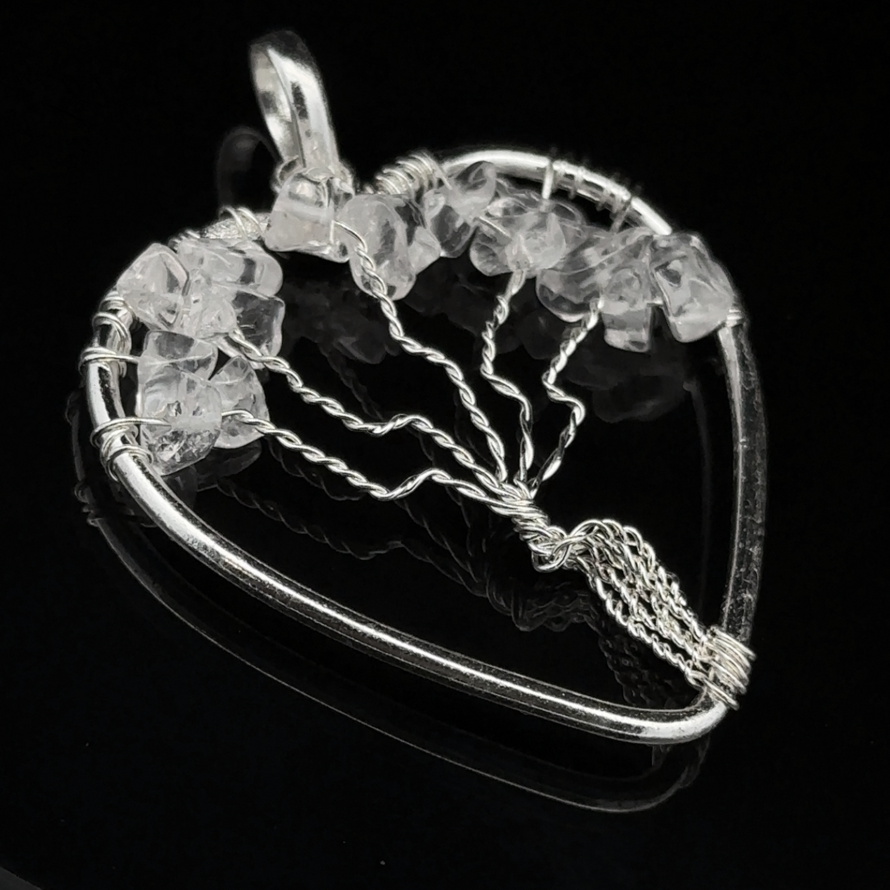 A Heart Shaped Tree of Life Pendant with an intricate design adorned with clear gemstones, set against a black background.