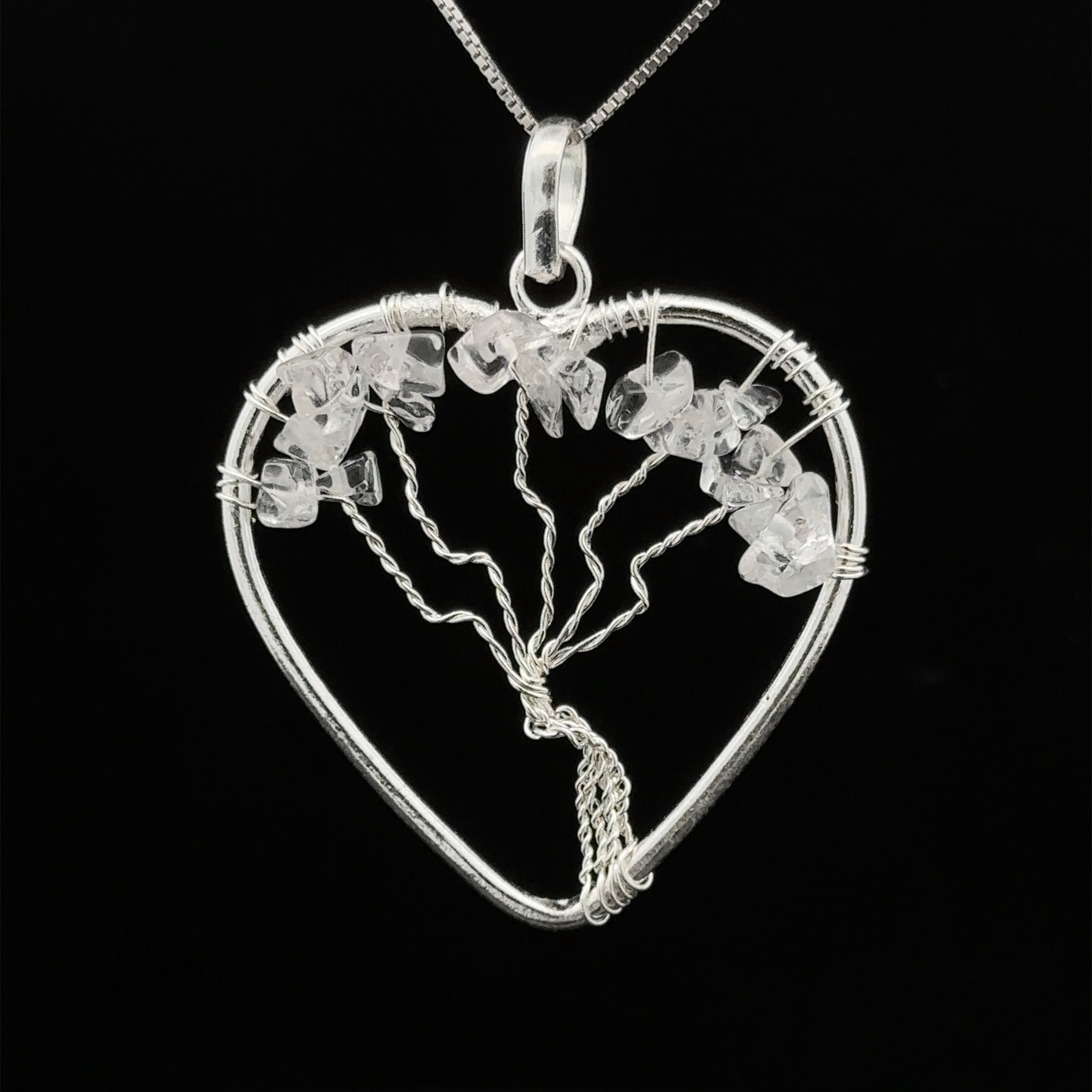 A Heart Shaped Tree of Life Pendant features a wire-wrapped tree design, adorned with small white stones and raw stone beads, all set against a black background.