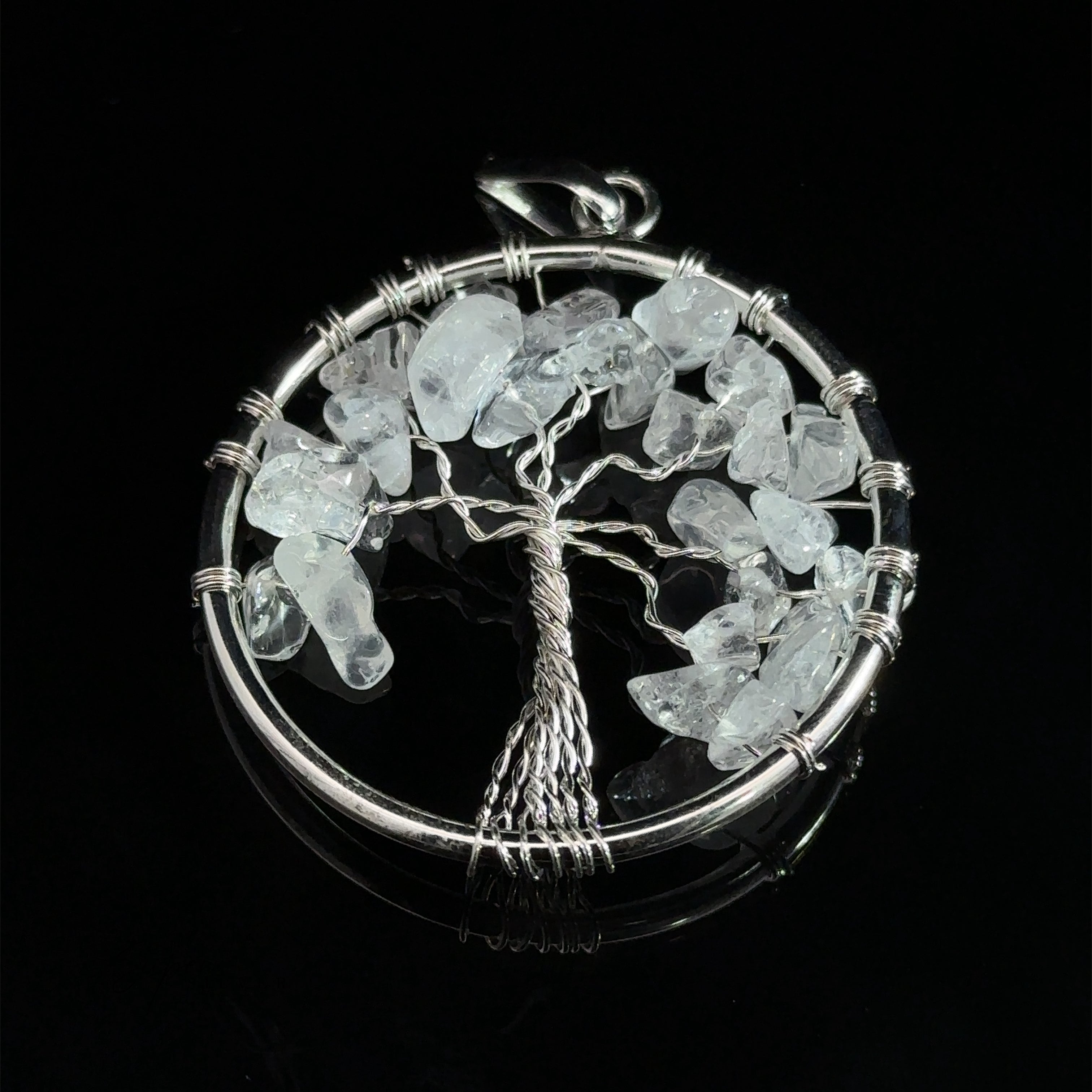 A stunning Wire Wrapped Tree of Life Pendant with Stones showcases a circular design with a wire-wrapped tree at its heart, adorned with translucent gemstones as leaves, all set against a black background.