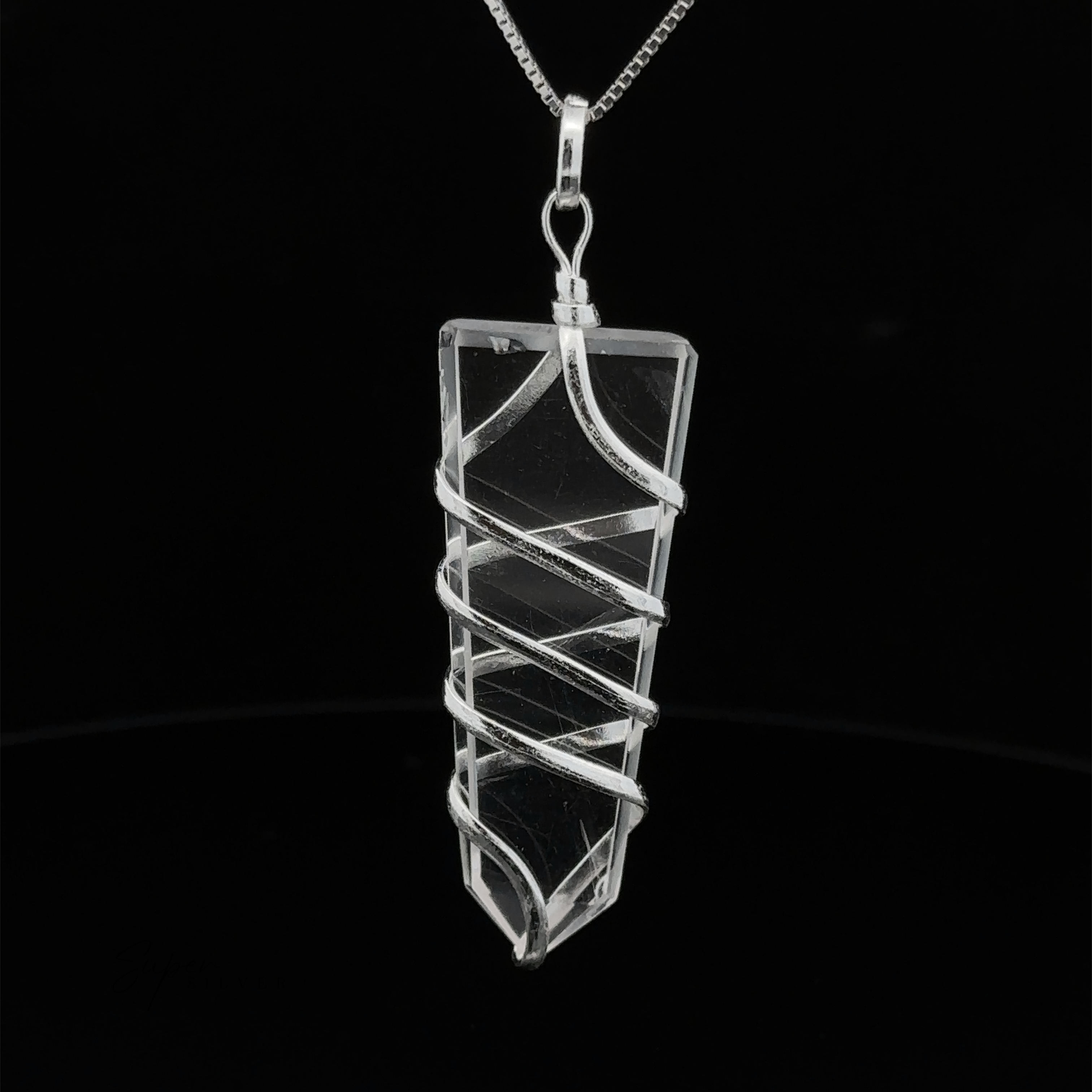A Wire Wrapped Slab Pendant in spiraled silver wire hangs from a thin silver chain against a black background, epitomizing exquisite gemstone jewelry.