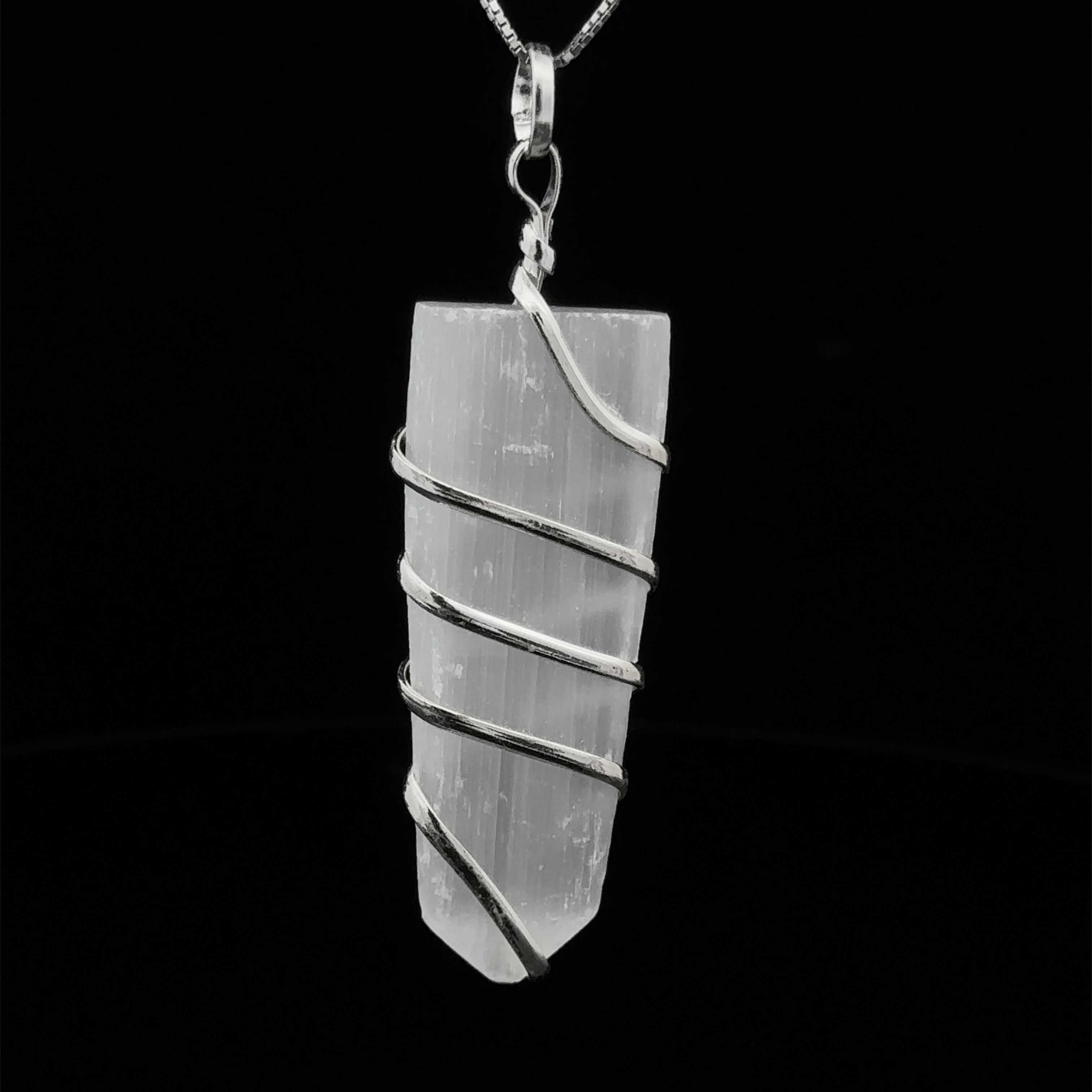 A Wire Wrapped Slab Pendant, hanging from a silver chain against a black background, exemplifies the allure of gemstone jewelry.