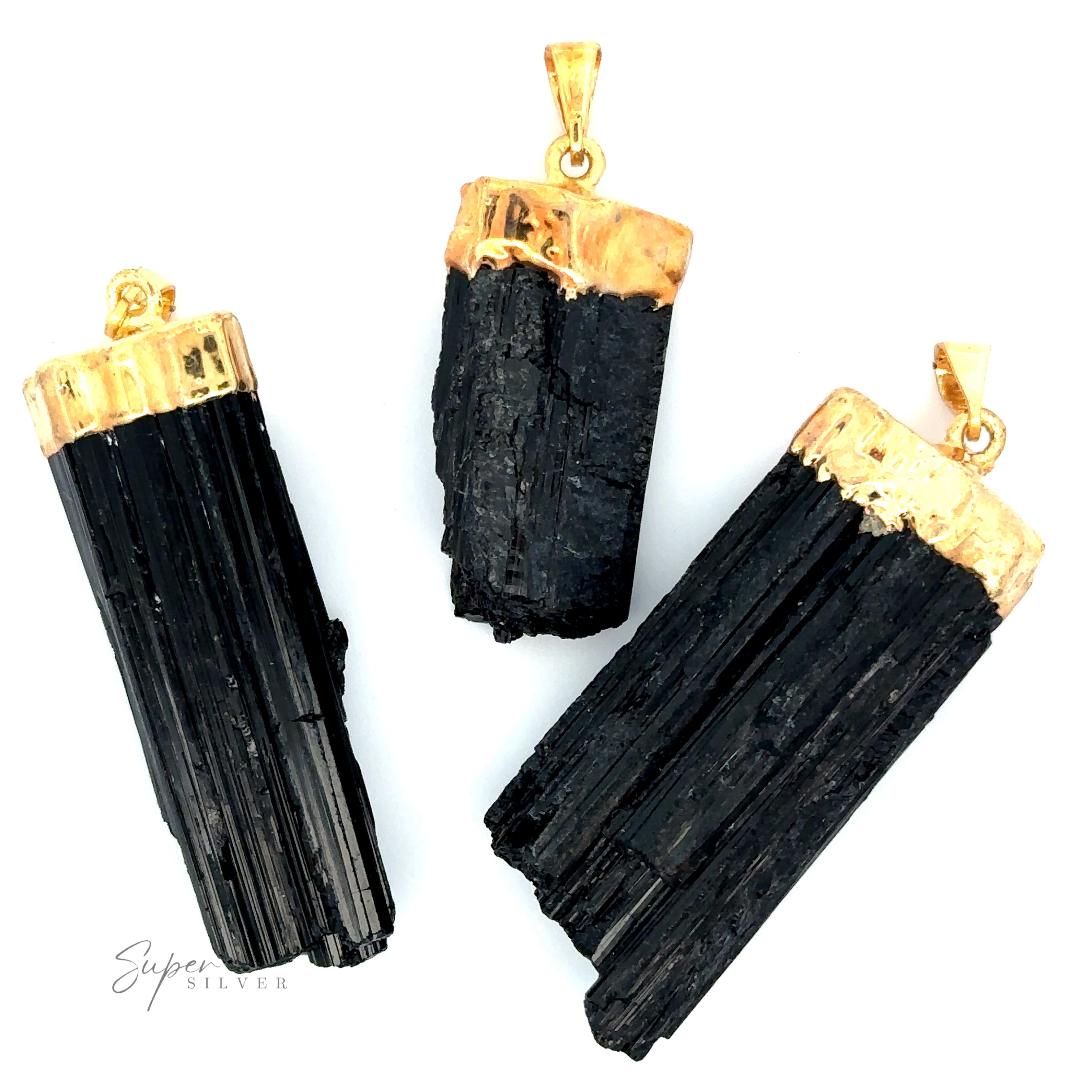 Three Raw Crystal Pendants With Gold Caps featuring natural gemstone pendants with raw black tourmaline crystals and gold-plated caps and bails, arranged on a white background. The image is credited to Super Silver in the corner.