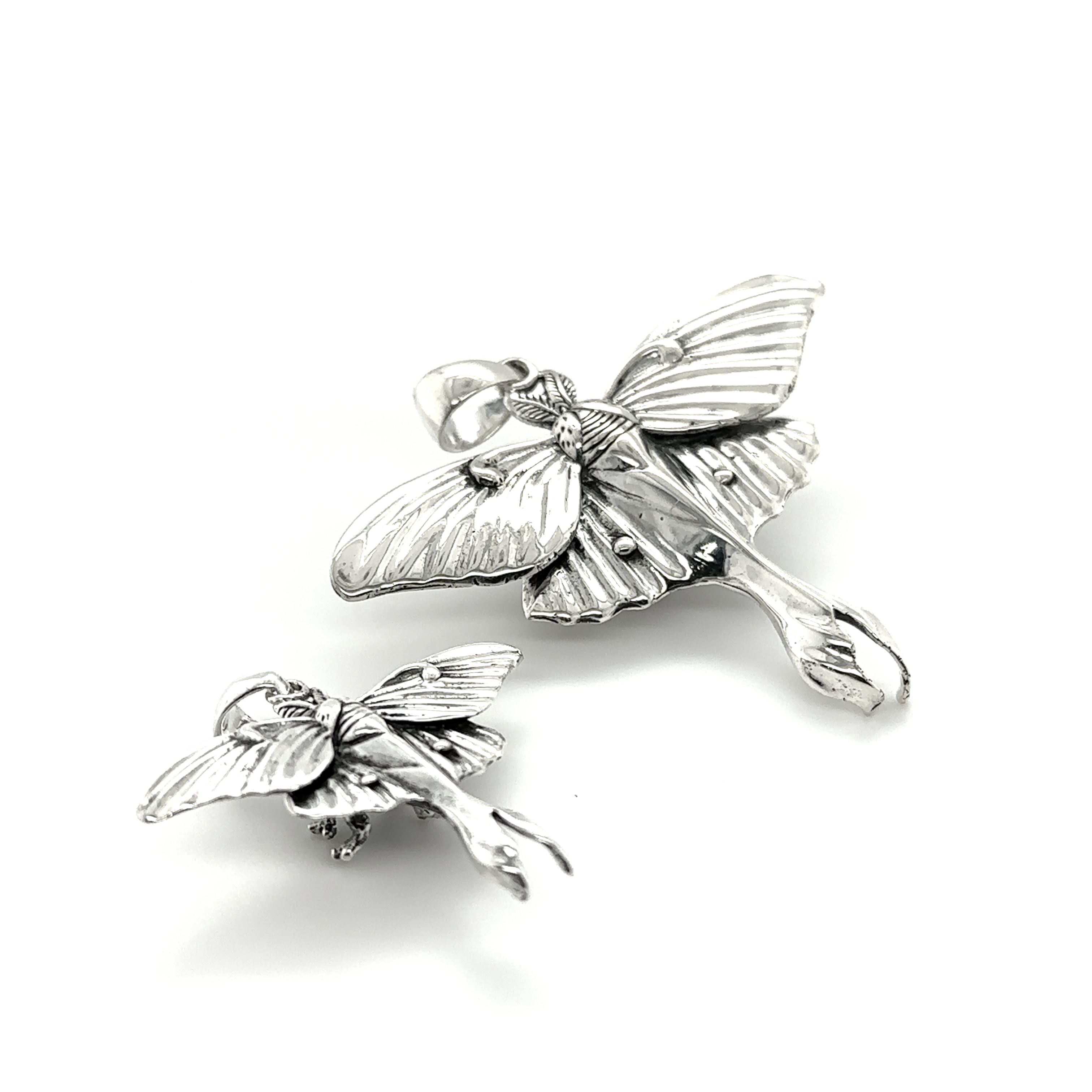 A pair of Super Silver Statement Lunar Moth Pendants on a white surface, exuding ethereal beauty.