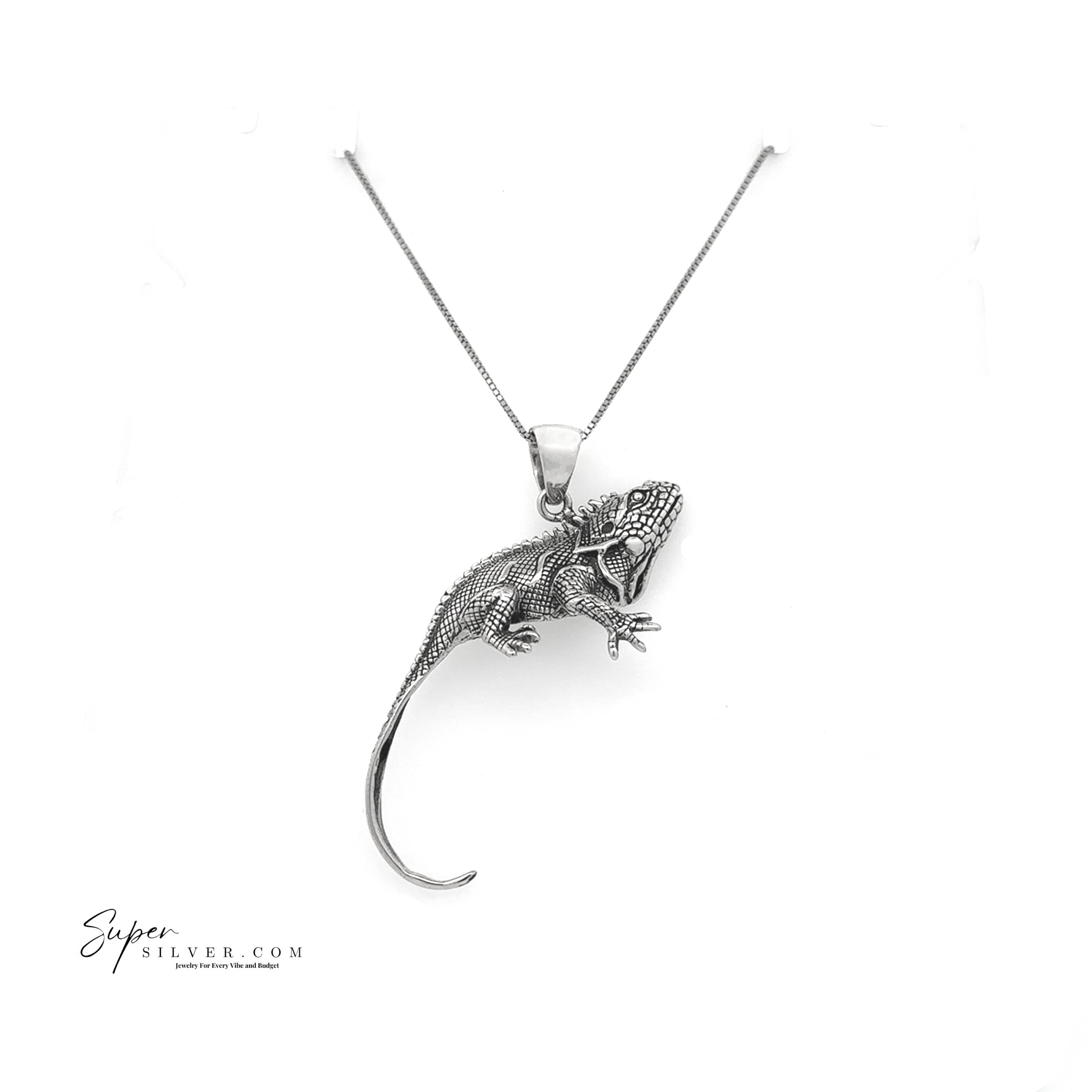 The Iguana Pendant from the Artssina Collection is a sterling silver, lizard-shaped piece hanging on a chain necklace and displayed against a white background.