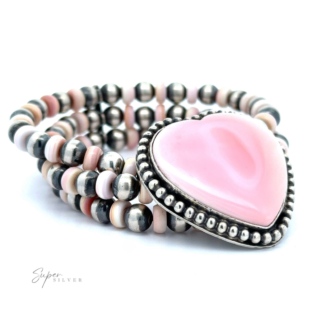 A multi-strand bracelet featuring Navajo pearl beads and a large, pink heart-shaped stone set in a detailed silver frame.
