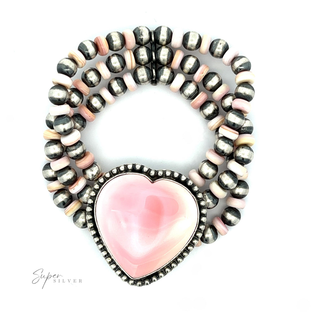 A bracelet composed of Navajo pearl beads shaped into a circle with a large pink conch heart charm in the center, set on a white background.