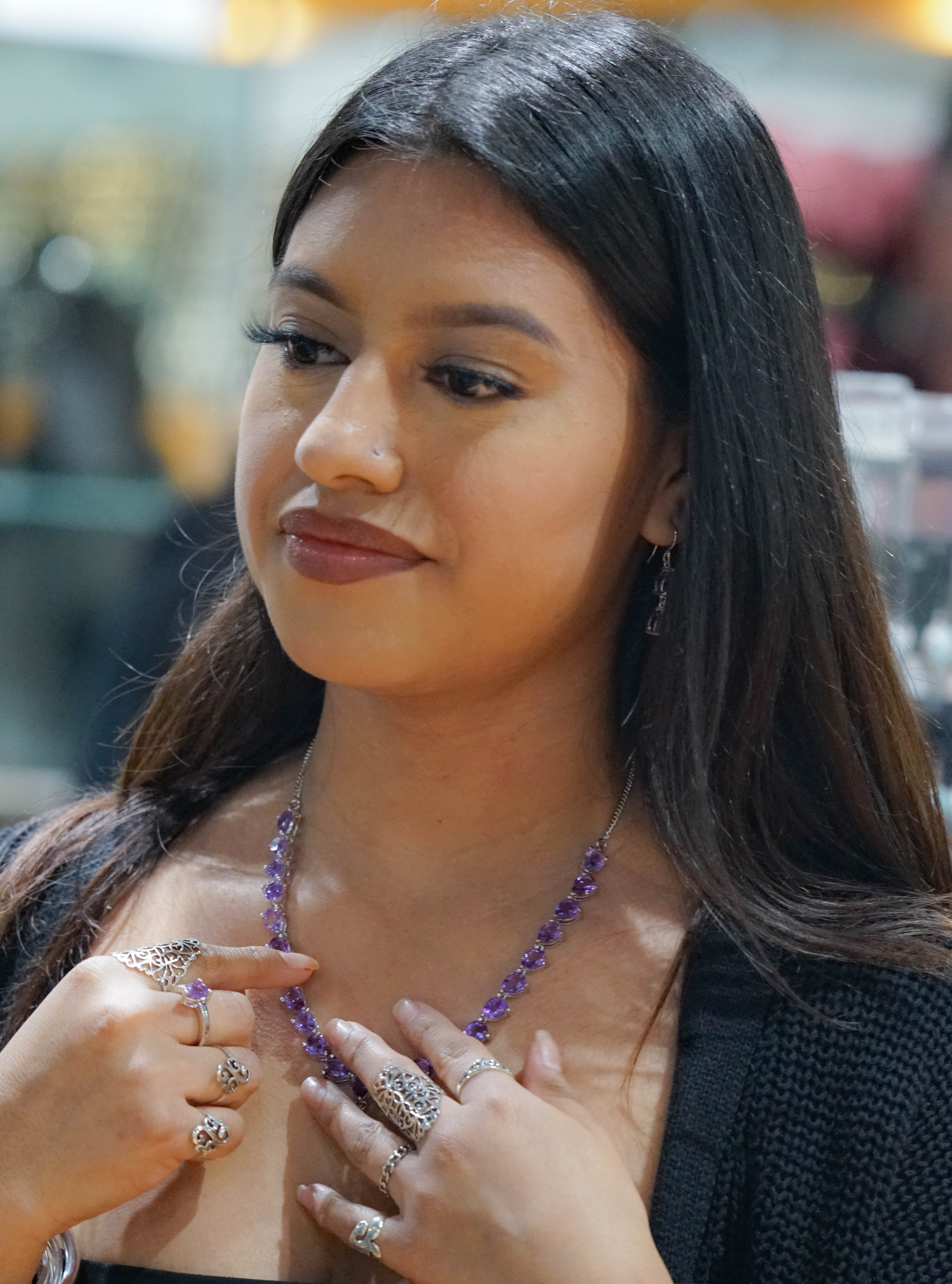 A woman examining an Elegant Faceted Gemstone Jewelry Set, smiling slightly in an indoor setting.