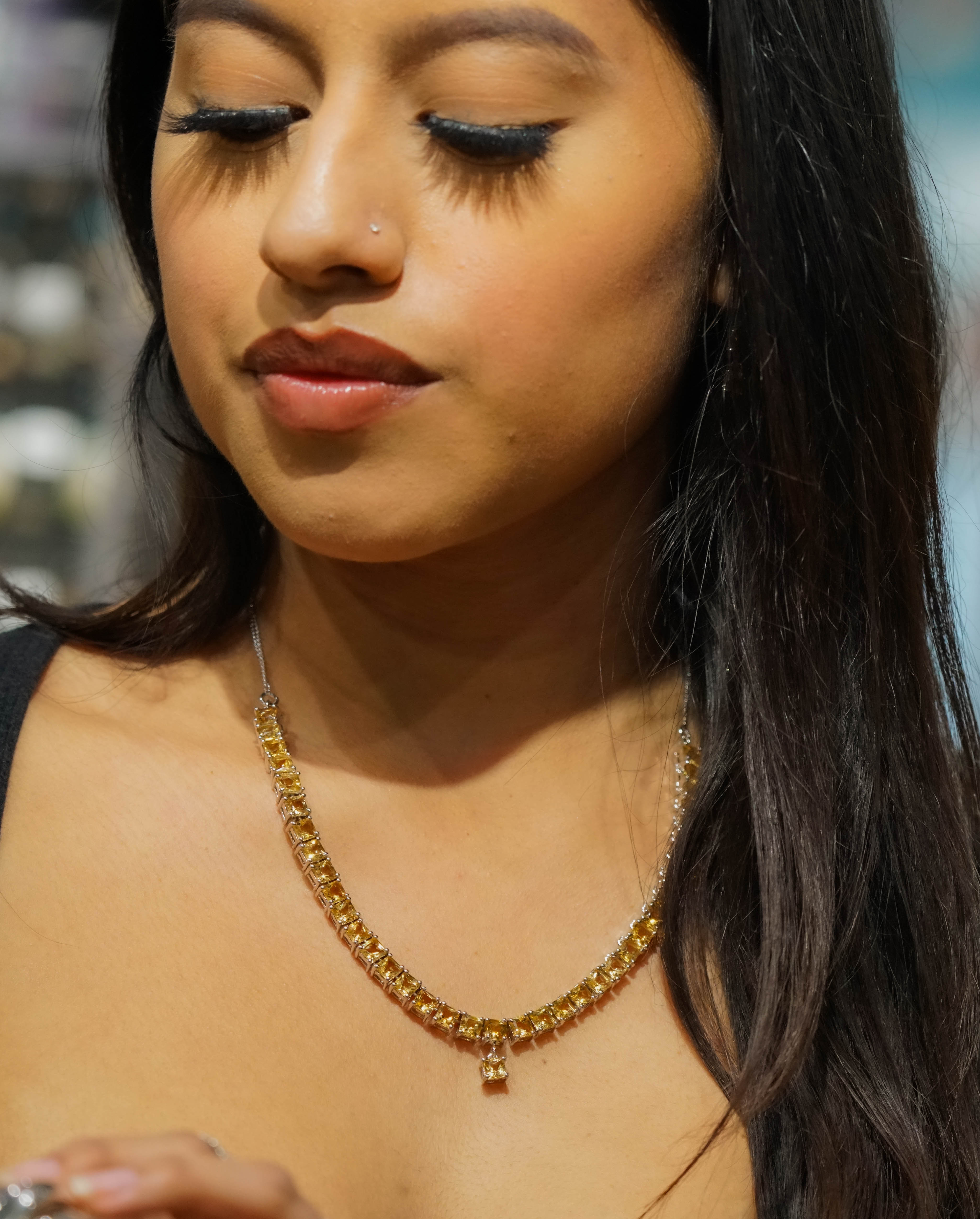 Close-up of a woman with long dark hair, wearing an Elegant Faceted Gemstone Jewelry Set, with her eyes closed and head slightly tilted.