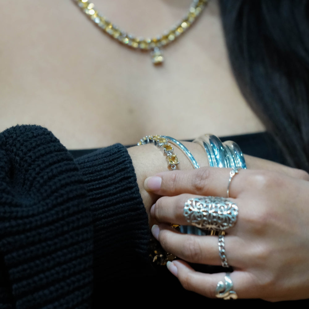 
                  
                    Close-up of a woman's hand adorned with an Elegant Faceted Gemstone Jewelry Set, touching her arm, with a gold necklace visible in the background.
                  
                