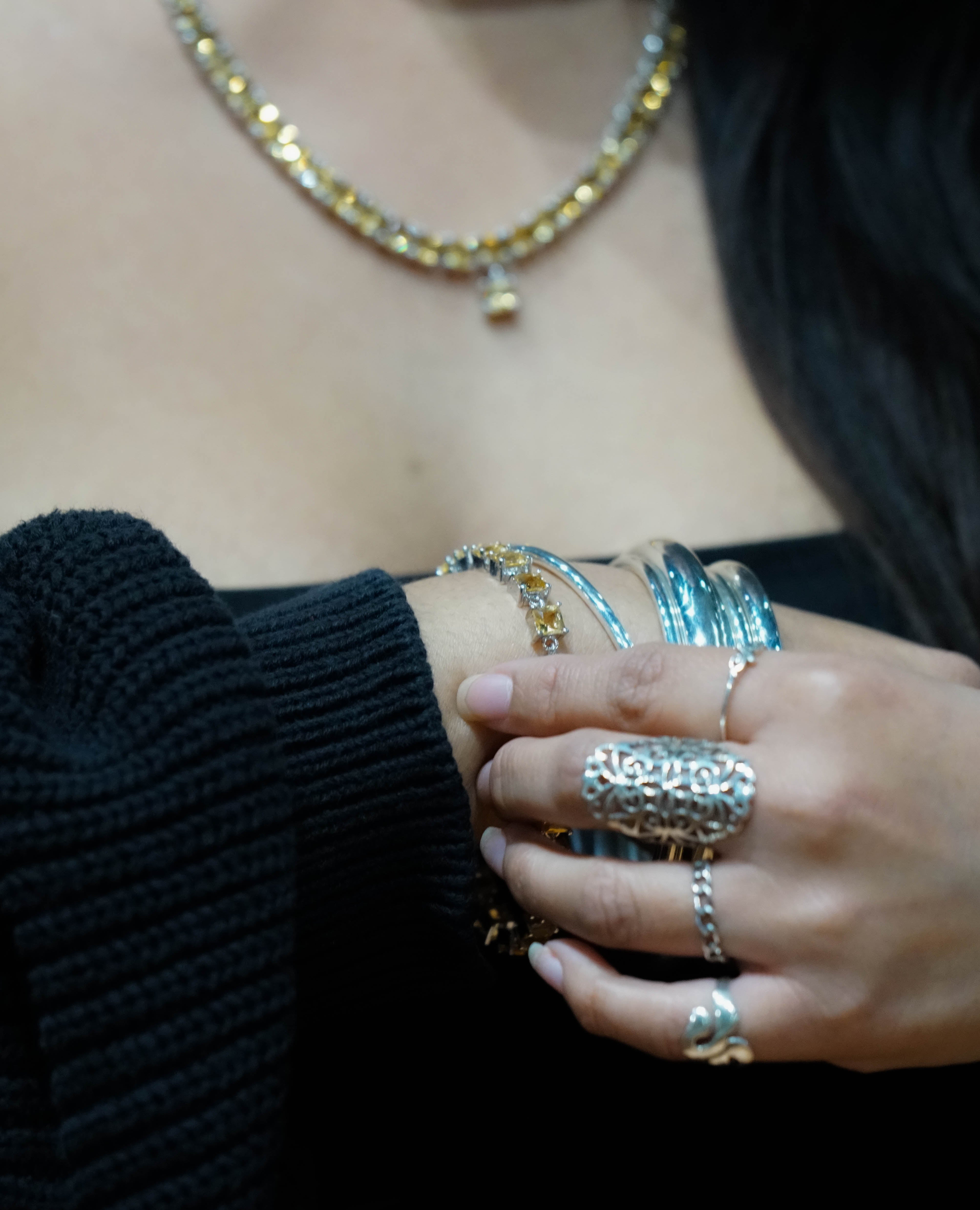 Close-up of a woman's hand adorned with an Elegant Faceted Gemstone Jewelry Set, touching her arm, with a gold necklace visible in the background.