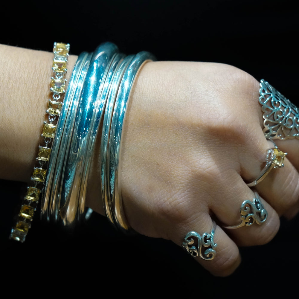 
                  
                    A woman's wrist adorned with multiple sterling silver bangles and an Elegant Faceted Gemstone Jewelry Set accented with small amethysts, set against a dark background.
                  
                