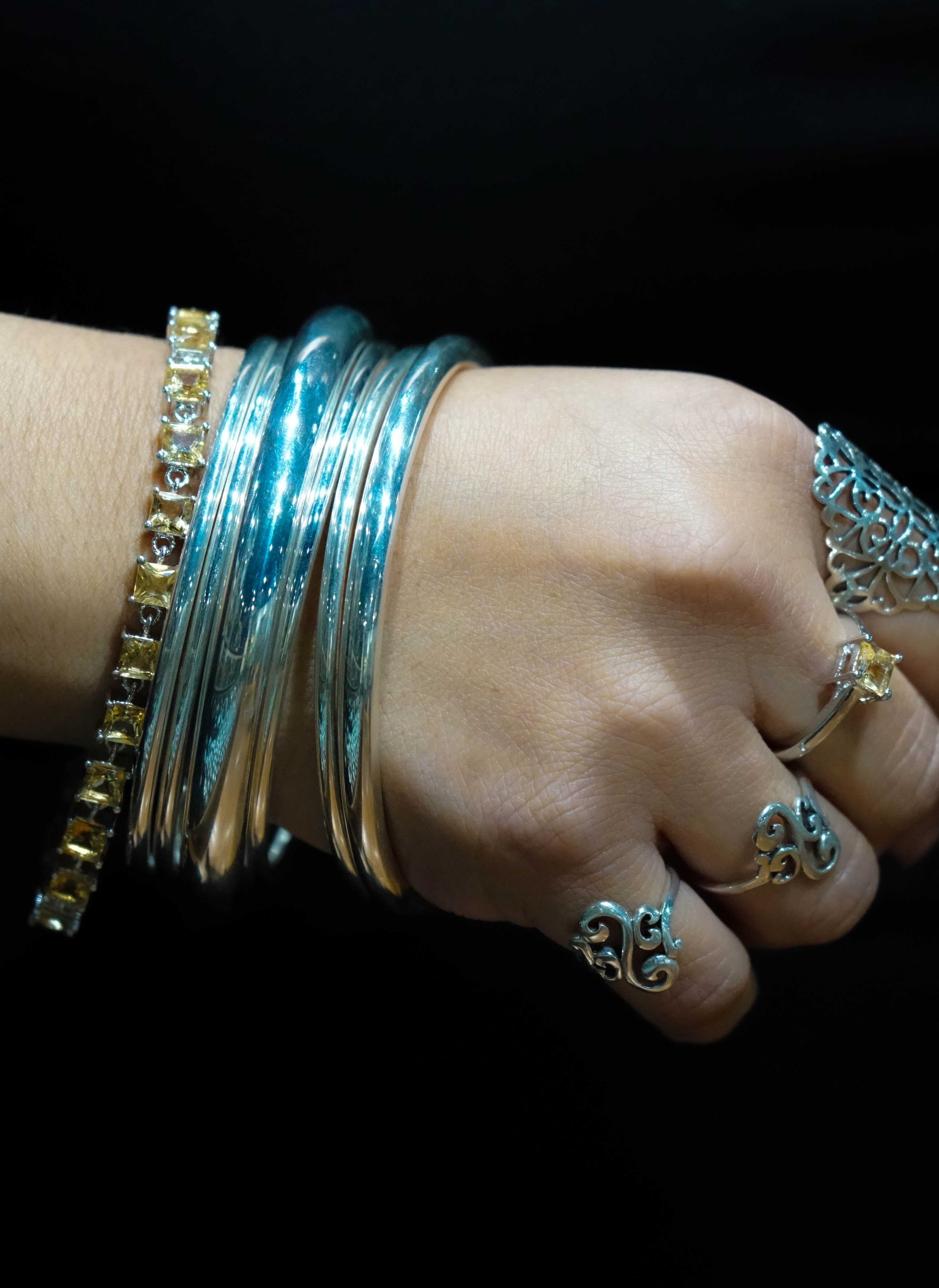 A woman's wrist adorned with multiple sterling silver bangles and an Elegant Faceted Gemstone Jewelry Set accented with small amethysts, set against a dark background.