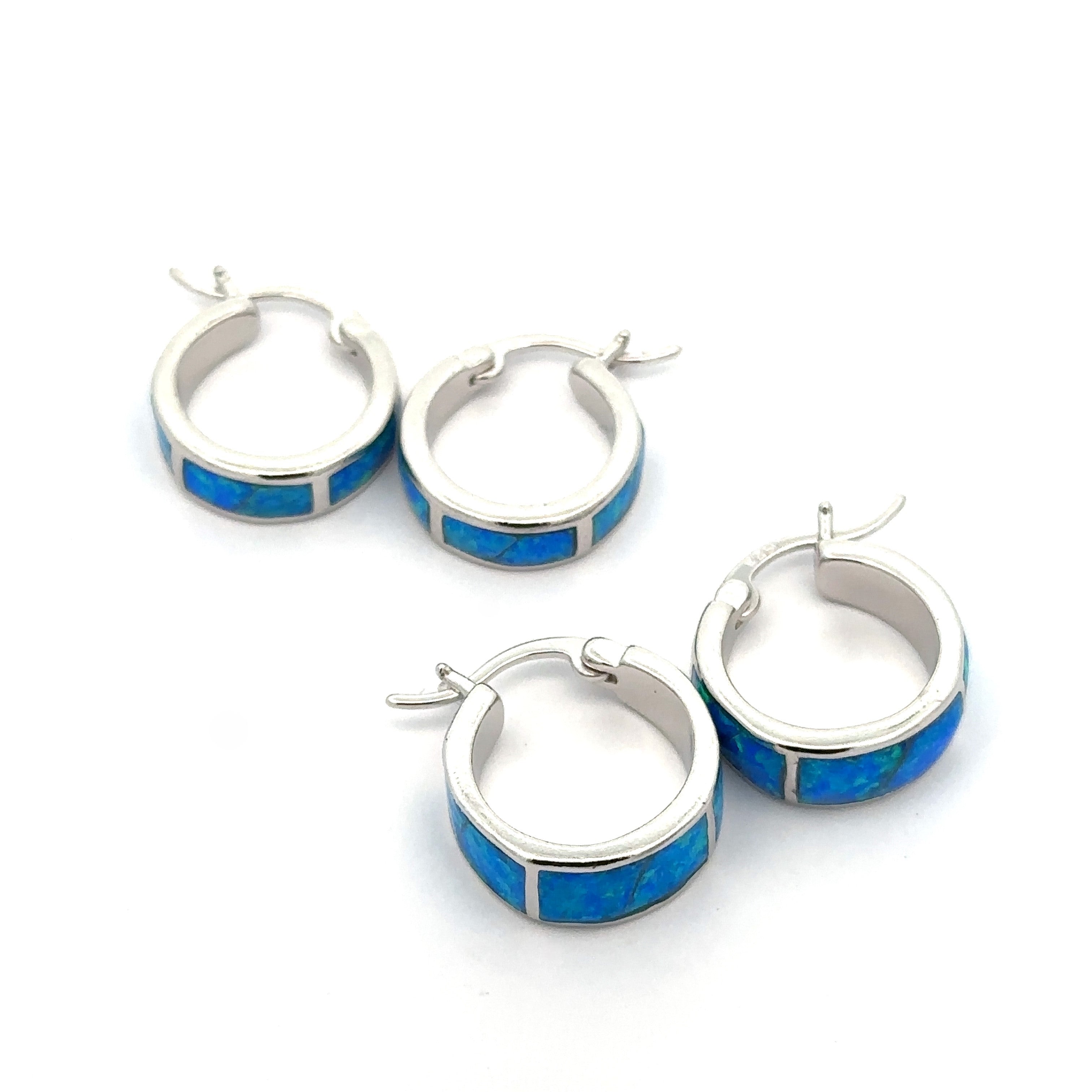 Four Blue Lab-Created Opal Huggie Hoop Earrings, featuring a striking blue lab-created opal inlay and a sleek rhodium finish, are arranged on a white background.