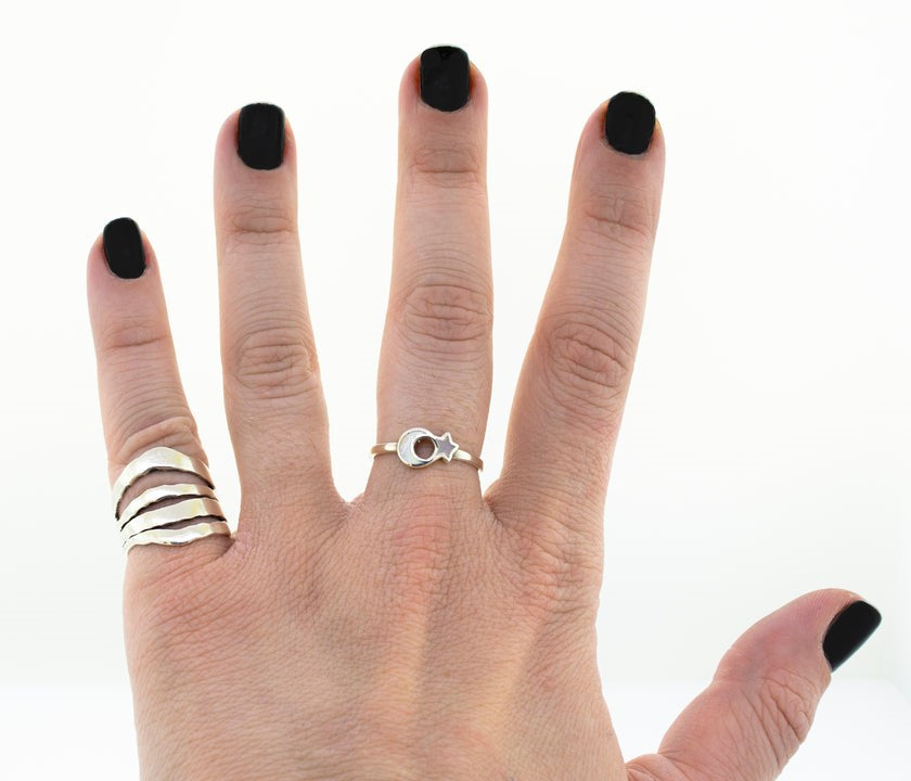 A hand with black nail polish displaying two rings, one the Crescent Moon And Star Ring with inlaid stones, and the other with an infinity symbol.