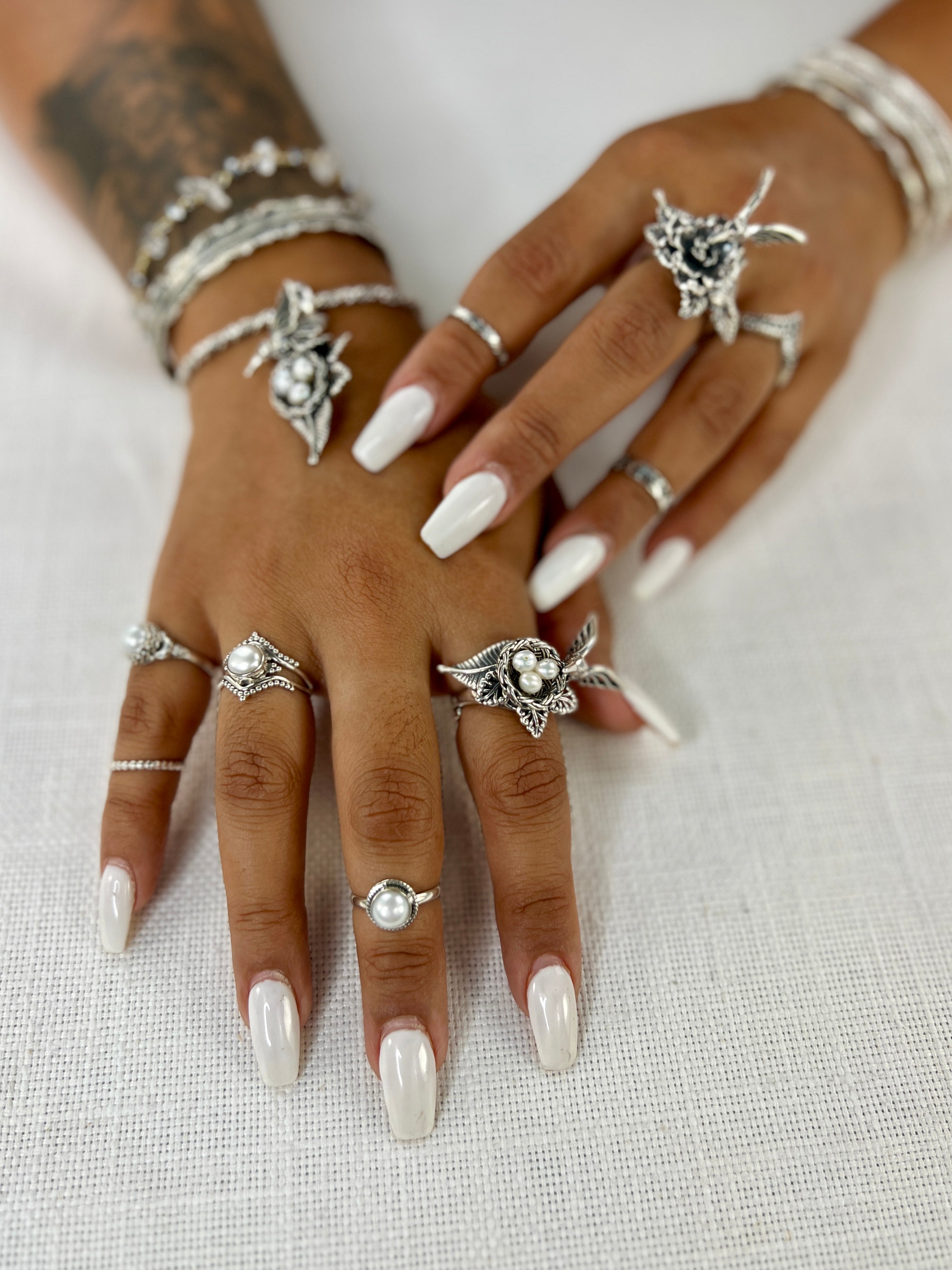 A woman's hands adorned with Super Silver rings, including one with the Hummingbird With Nest of Pearls Ring design, as well as a timeless pearl ring.