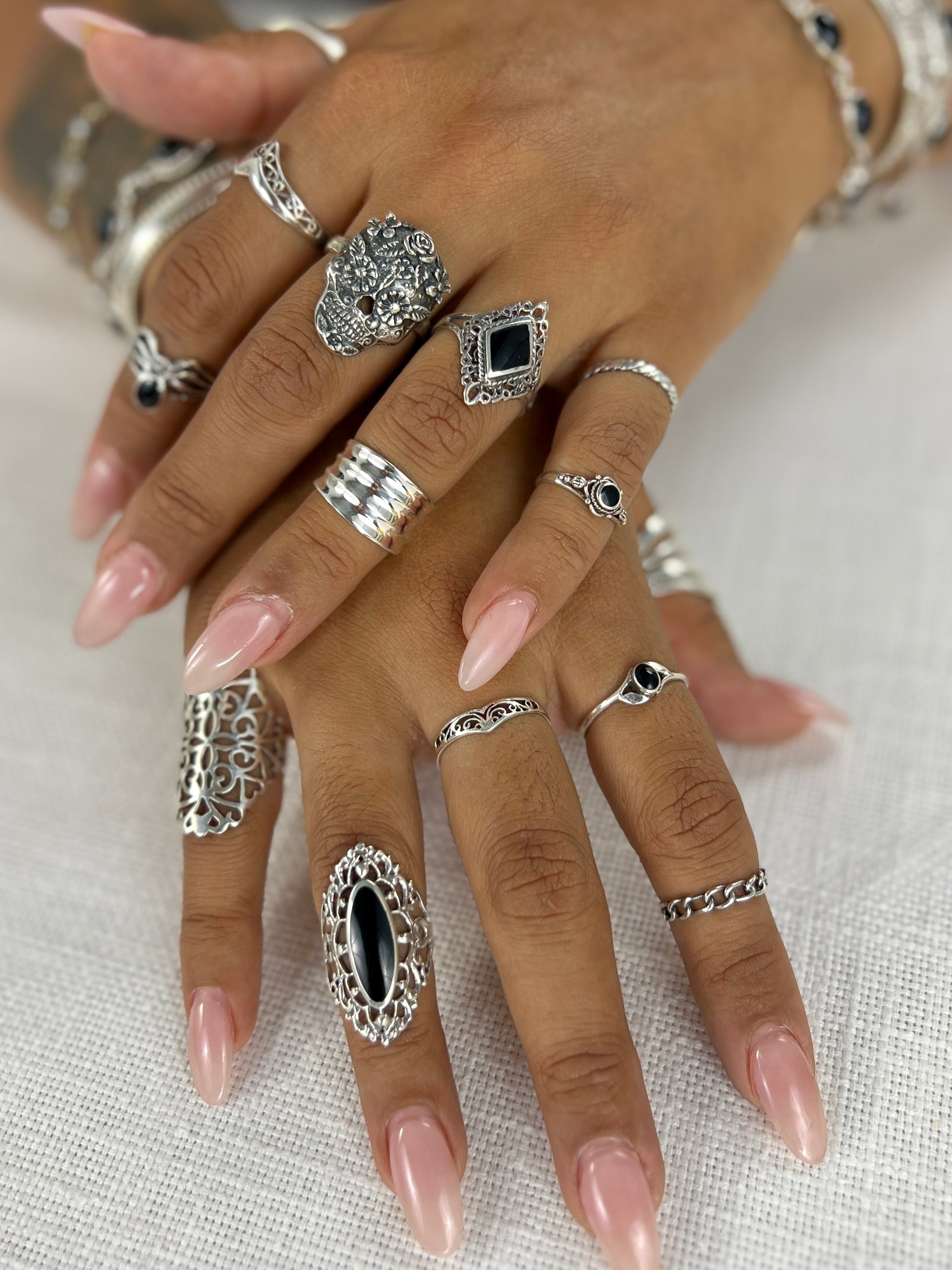 A woman's hands adorned with a Super Silver Diamond Shaped Filigree Ring with Inlaid Stones and a variety of rings, including lacy filigree and midi-rings.