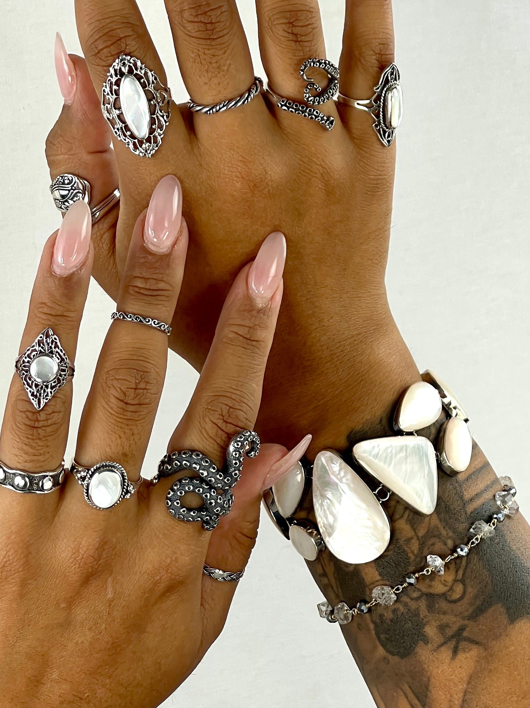 A woman's hand adorned with a luminous Super Silver Statement Mother of Pearl Bracelet and a statement bracelet.