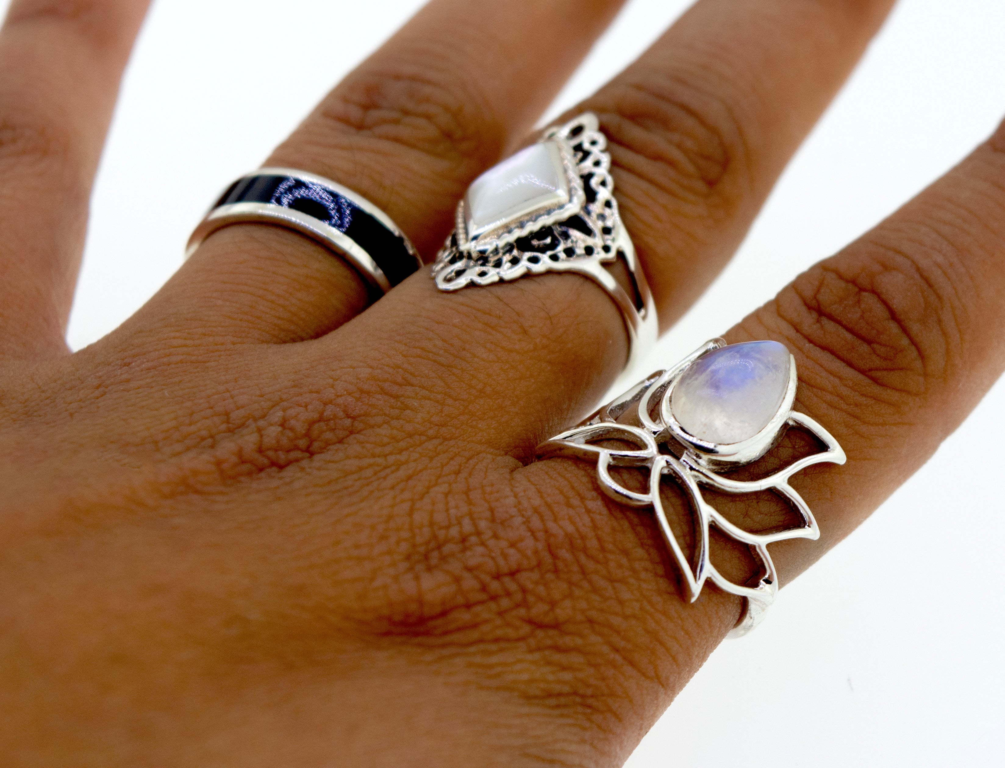 Close-up of a hand wearing three unique Online Exclusive Teardrop Stone Lotus Rings on different fingers, set against a plain white background.
