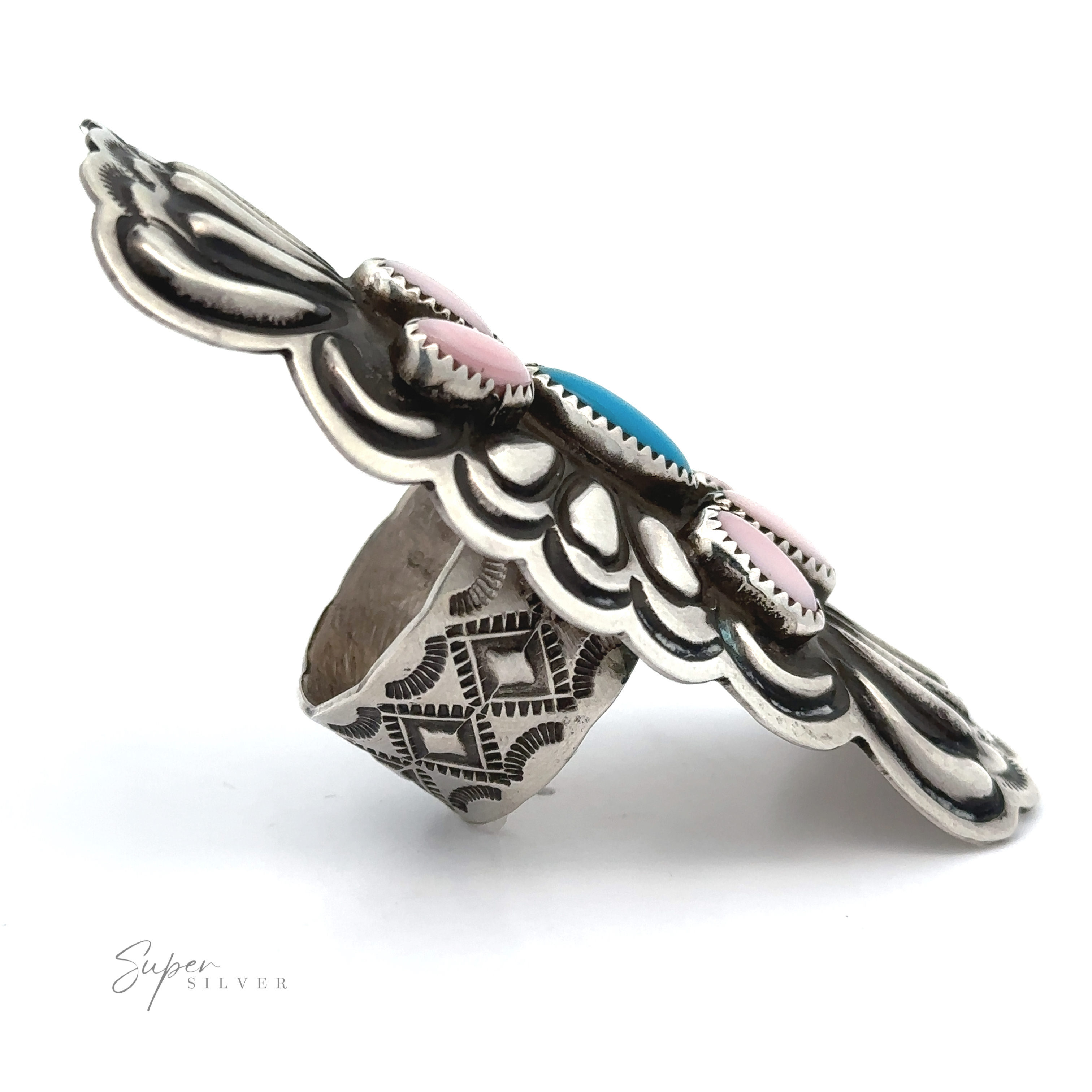 The Blush and Thunder Ring features a wide sterling silver band with intricate engravings, scalloped edges, and pink and blue stones at its center—artfully photographed on white, evoking Native American jewelry design.