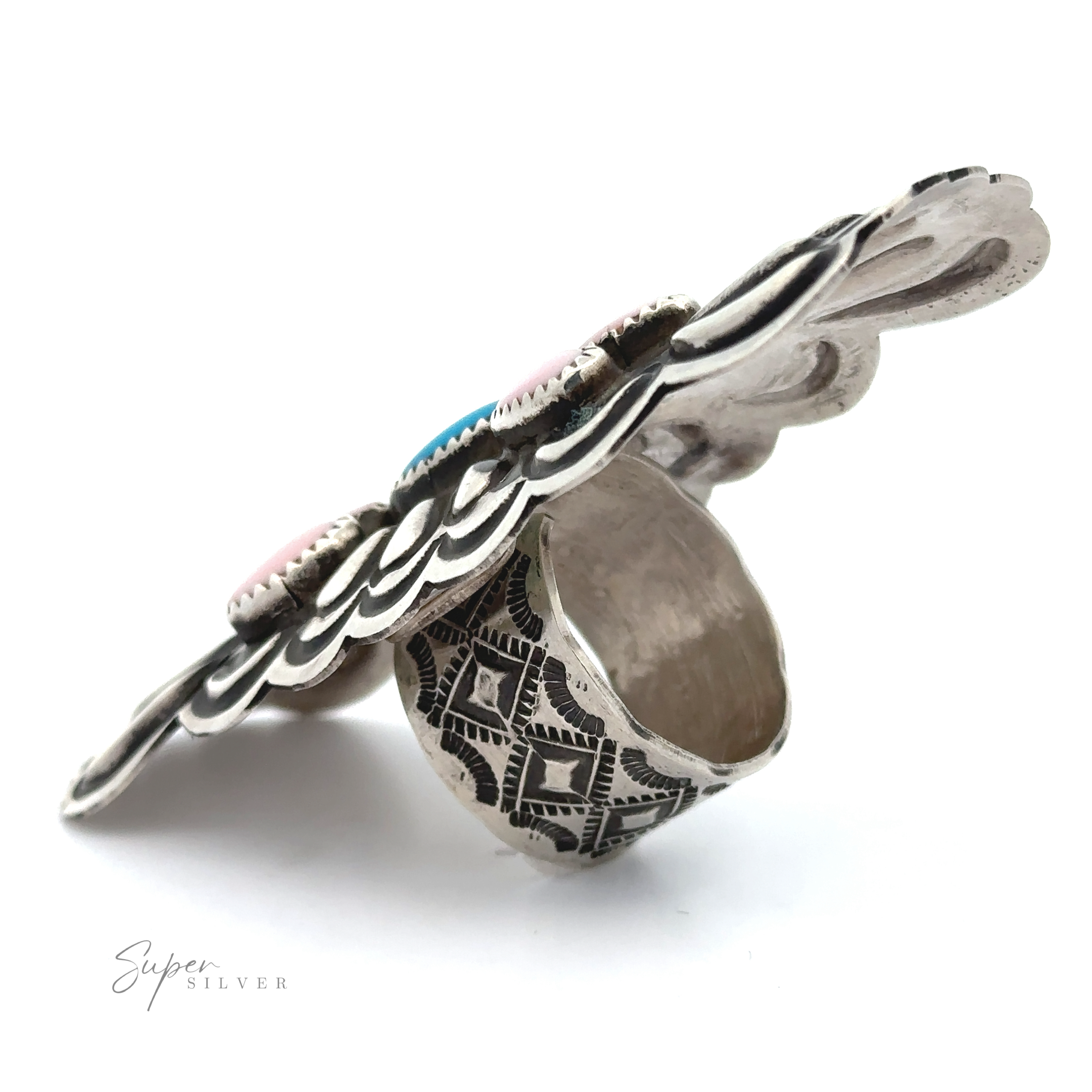 The Blush and Thunder Ring features a wide sterling silver band with engraved details and a bold, scalloped top accented by turquoise and pink stones. Inspired by Native American jewelry, this statement ring stands out against a white background.