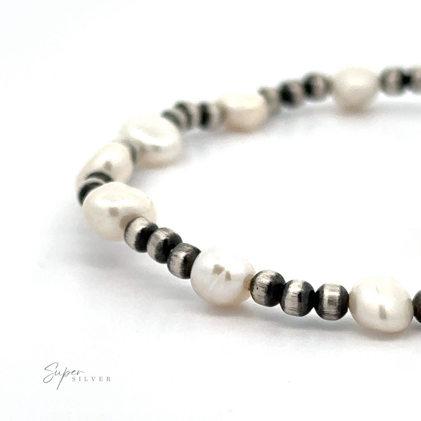 
                  
                    Close-up of a Native American Beaded Pearl Bracelet made of alternating white pearl-like and small metallic beads against a white background.
                  
                