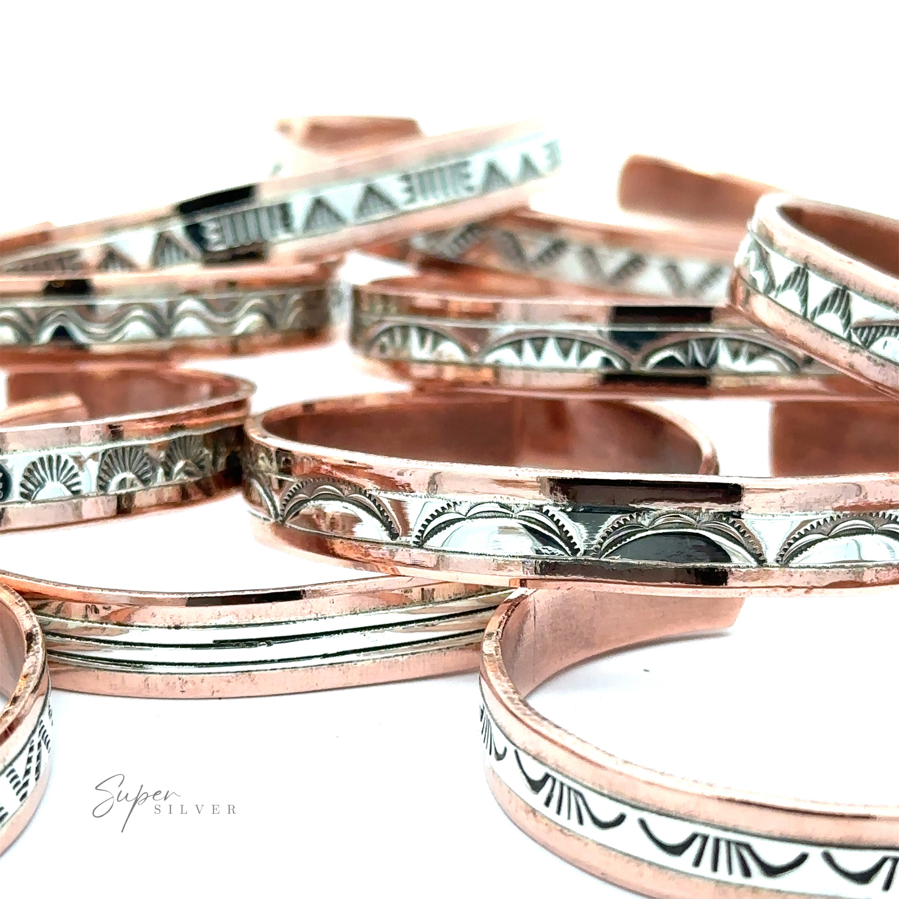 A collection of Native American Handmade Copper And Silver Bracelets with intricate geometric designs arranged on a white surface.