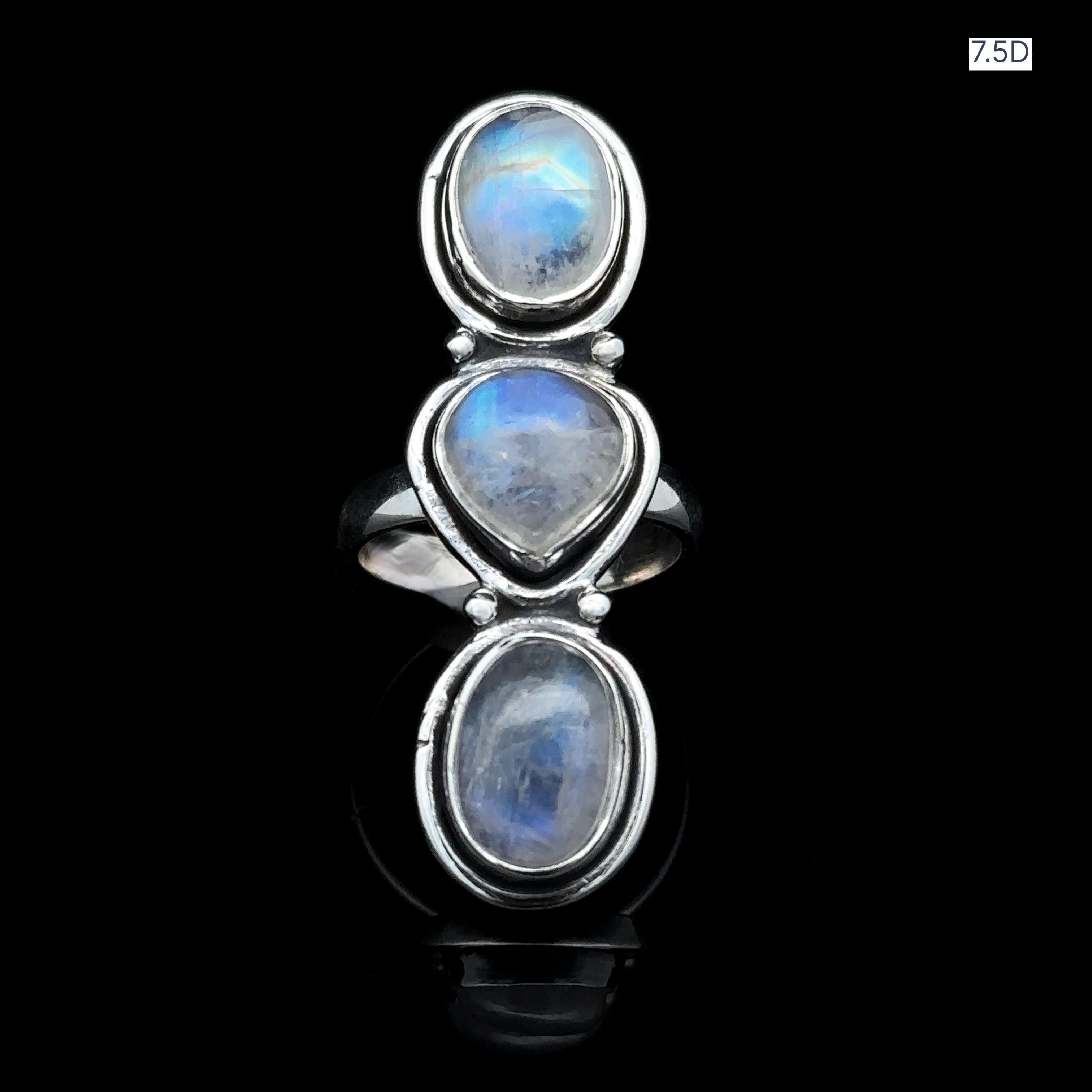 The Triple Moonstone Ring, crafted from sterling silver and showcasing three oval moonstones aligned on a black backdrop, emanates goddess energy. The label "7.5D" is positioned in the top right corner.