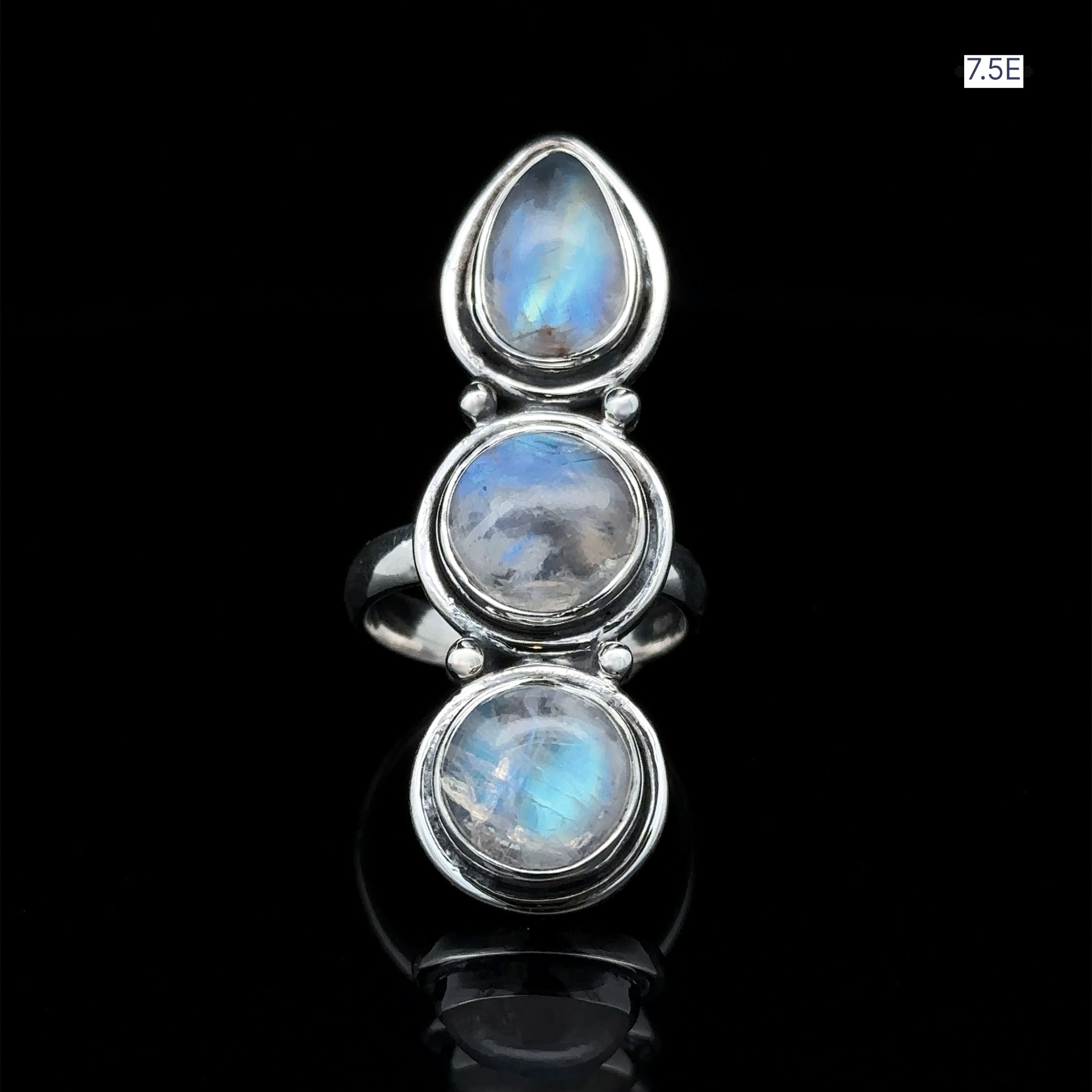 The "Triple Moonstone Ring," crafted from sterling silver and featuring three oval moonstones, radiates goddess energy against a dark background. The size label "7.5E" is positioned in the top right corner.