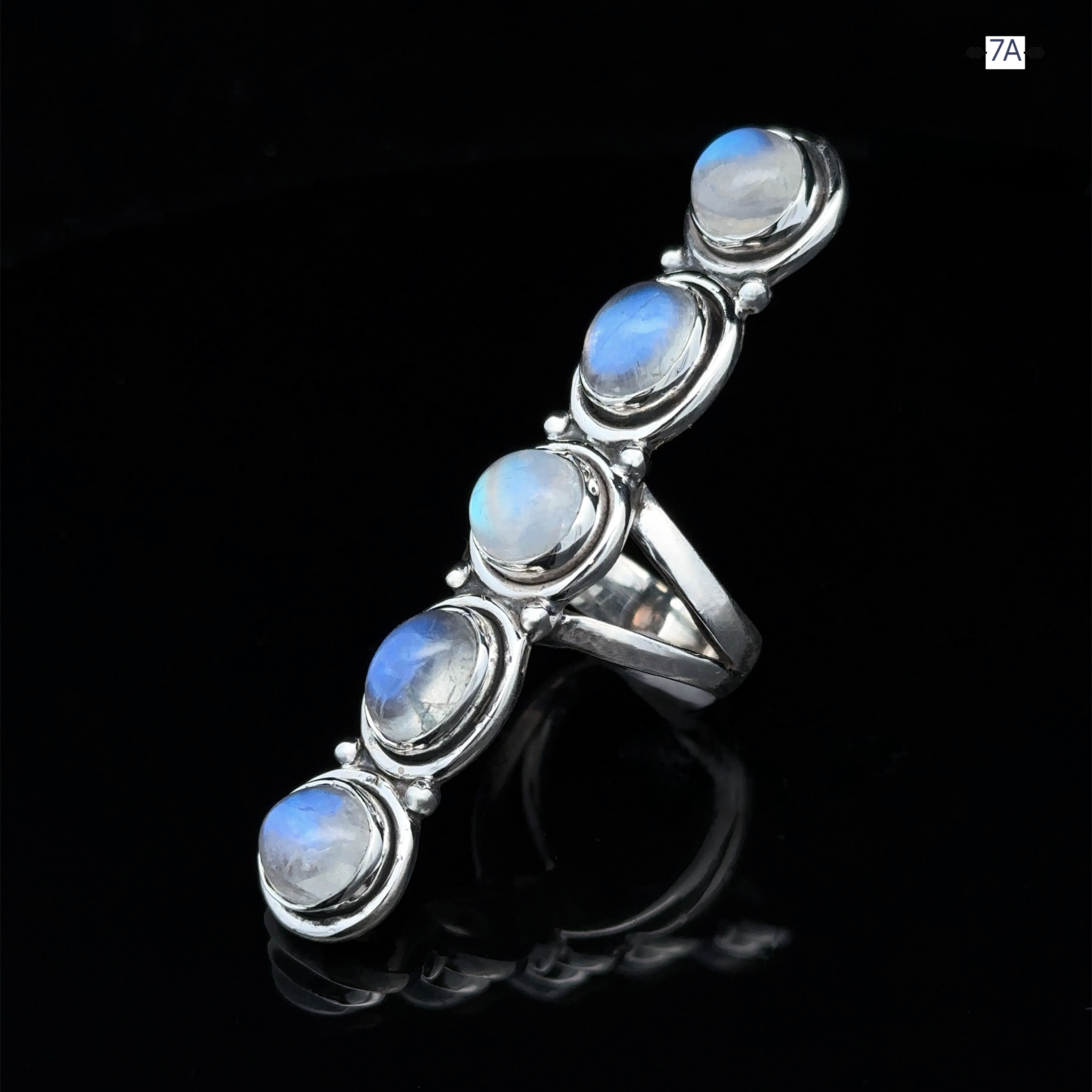 The Moonstone Ladder Ring is a Bohemian-style piece crafted from sterling silver, showcasing five round blue moonstones set in a vertical line on a glossy black background.